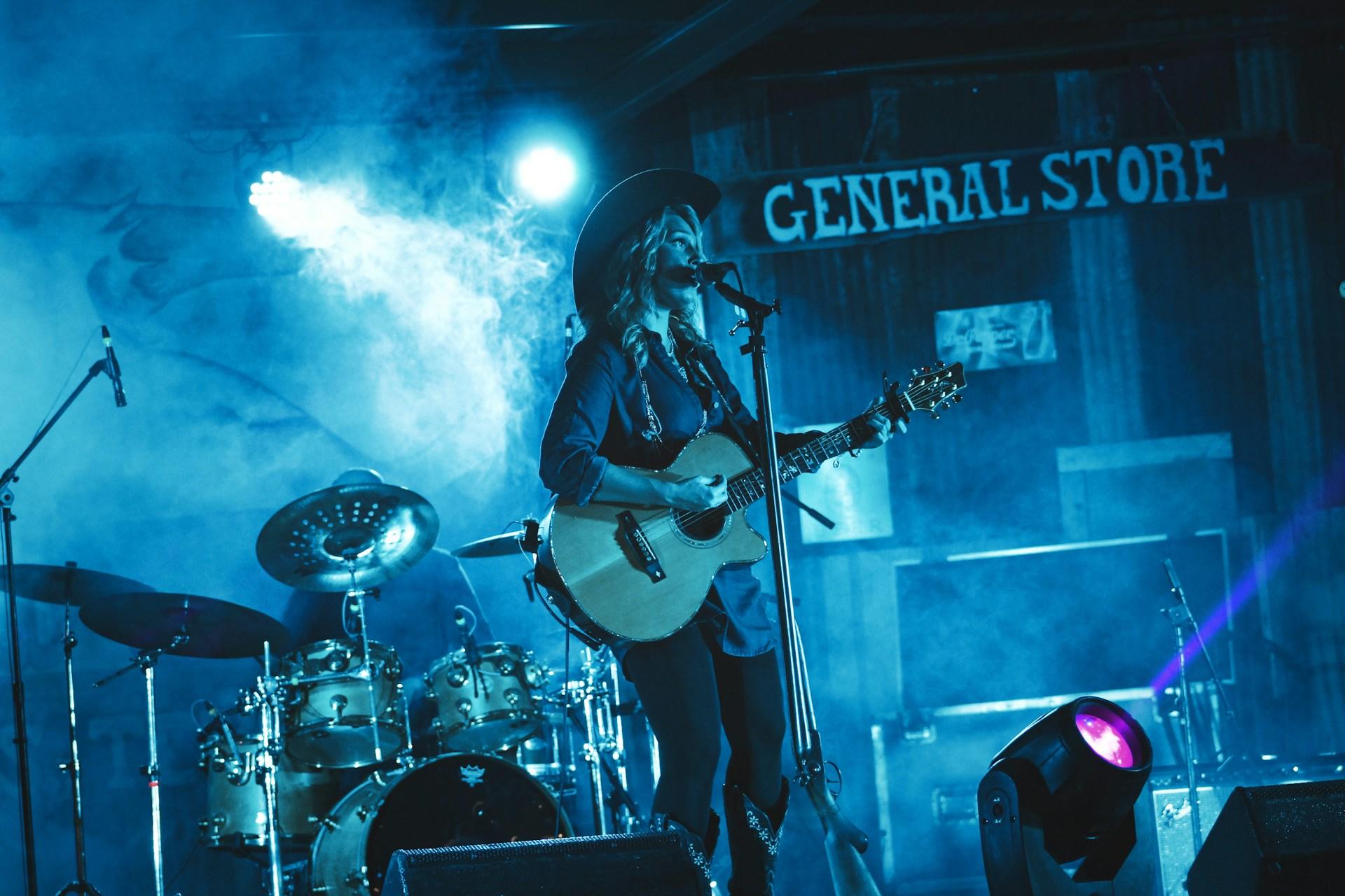 a woman singing country music with a guitar on stage, there are blue lights shining on her