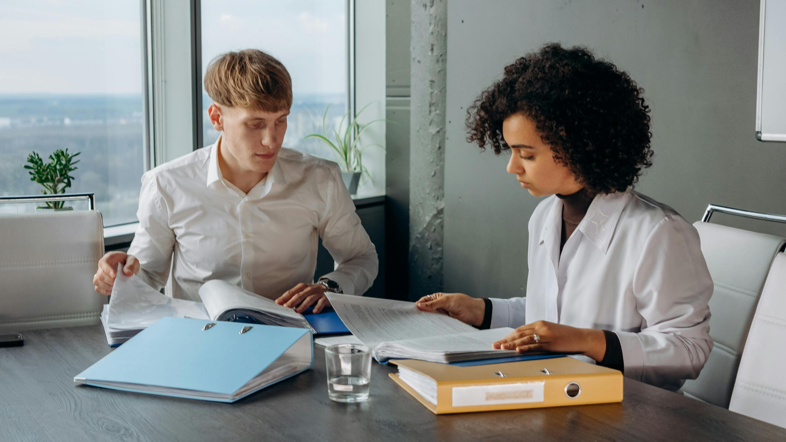 Colleagues in white long-sleeve shirts sitting and reading requirements in a conference room
