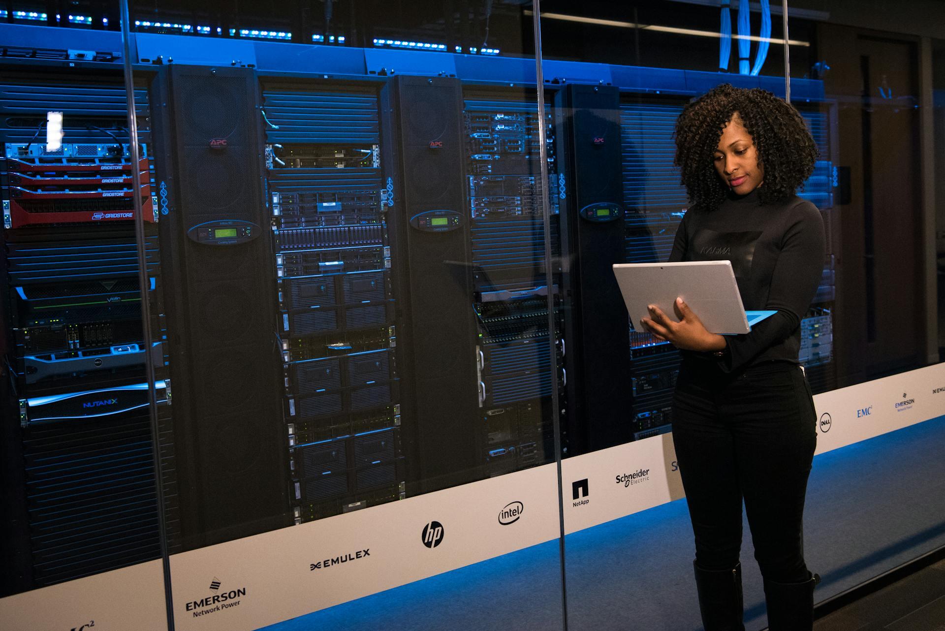 A data scientist engineer stands in front of servers with a laptop.