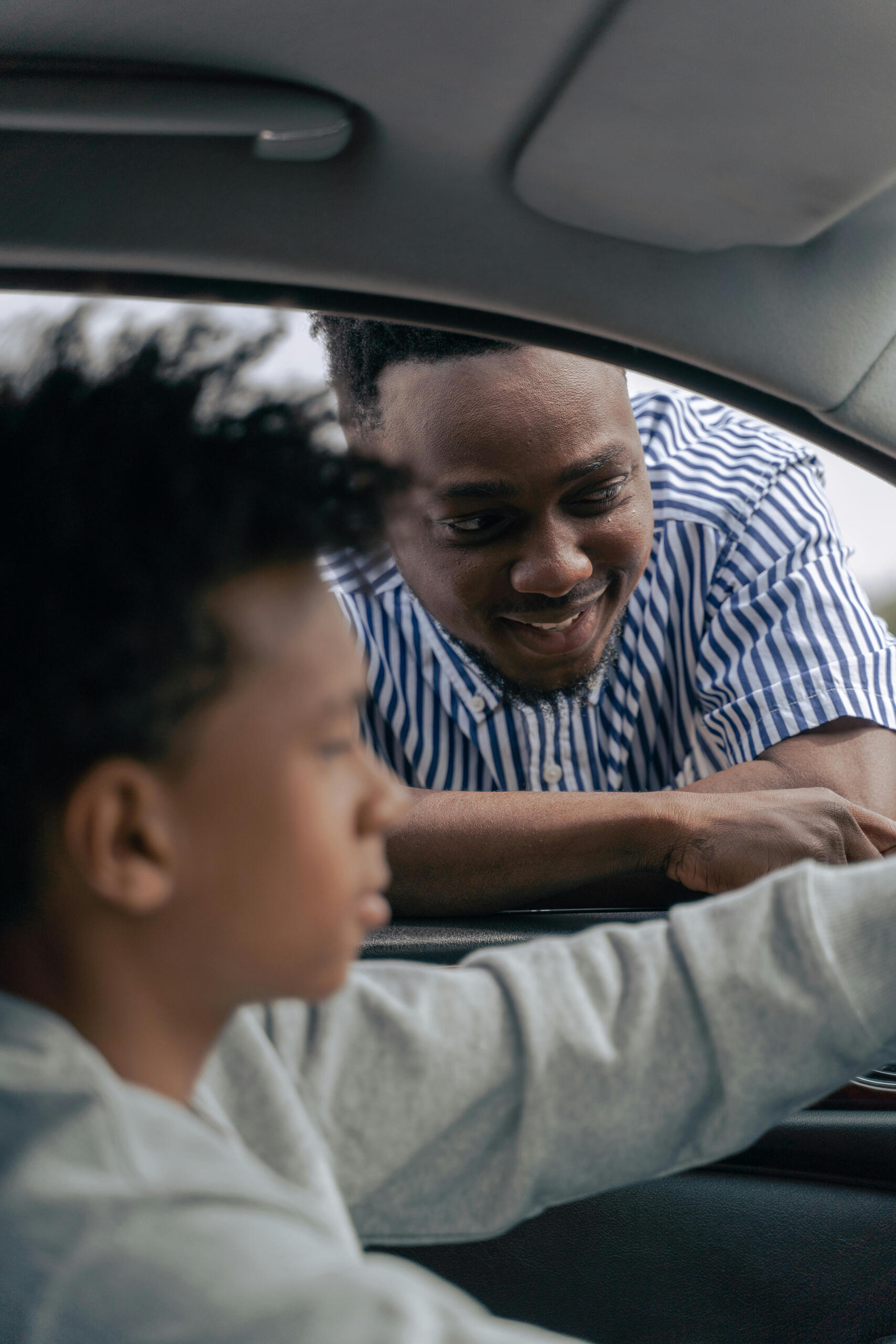 Man in blue and white striped shirt supervising driver in car