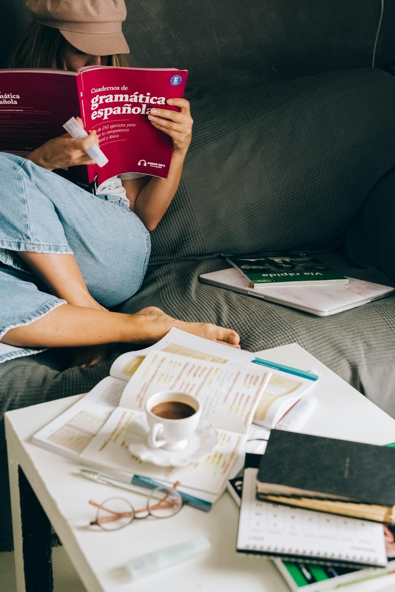 A woman on a couch reads a Spanish Grammar book