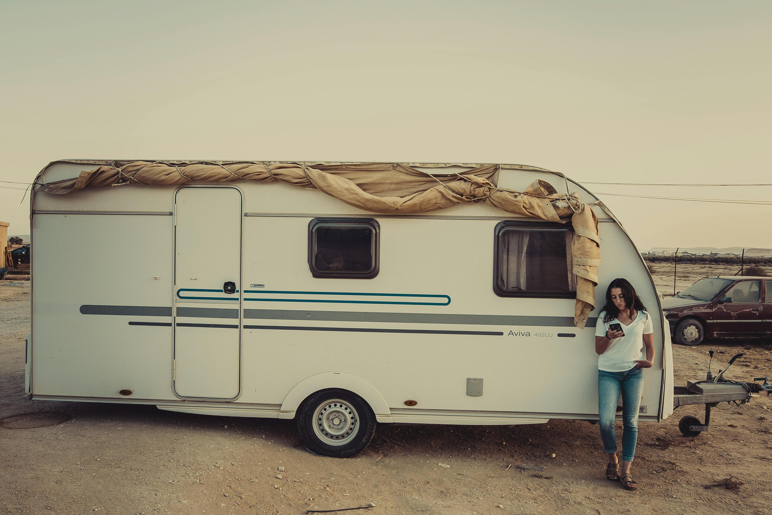 Woman wearing white crew-neck shirt leaning on RV trailer