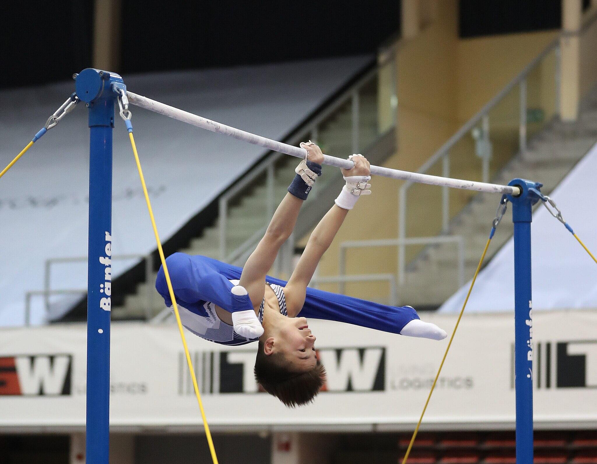 A little kid hanging on the horizontal bar.