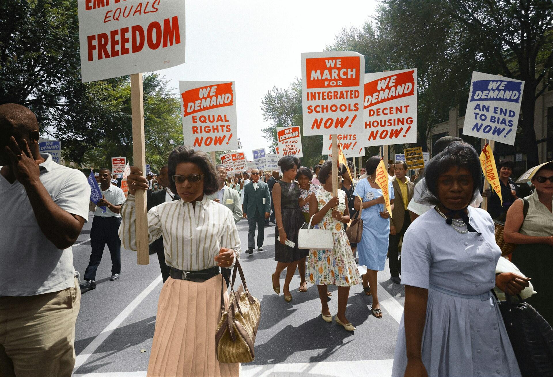 a colorized photo of civil rights protesters marching and holding signs promoting integration