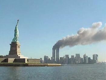 A photo of the Twin Towers billowing smoke into he sky with the Statue of Liberty in the foreground.