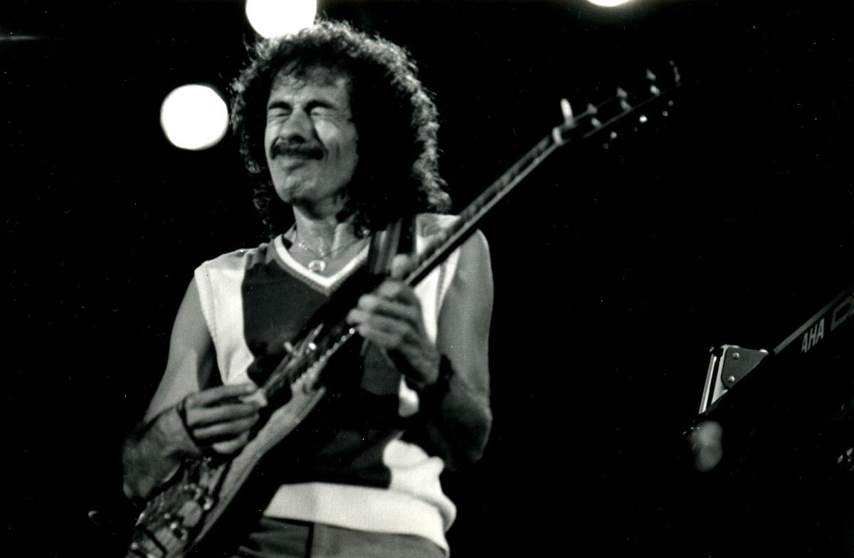 A black and white photo of Carlos Santana playing the guitar on stage.
