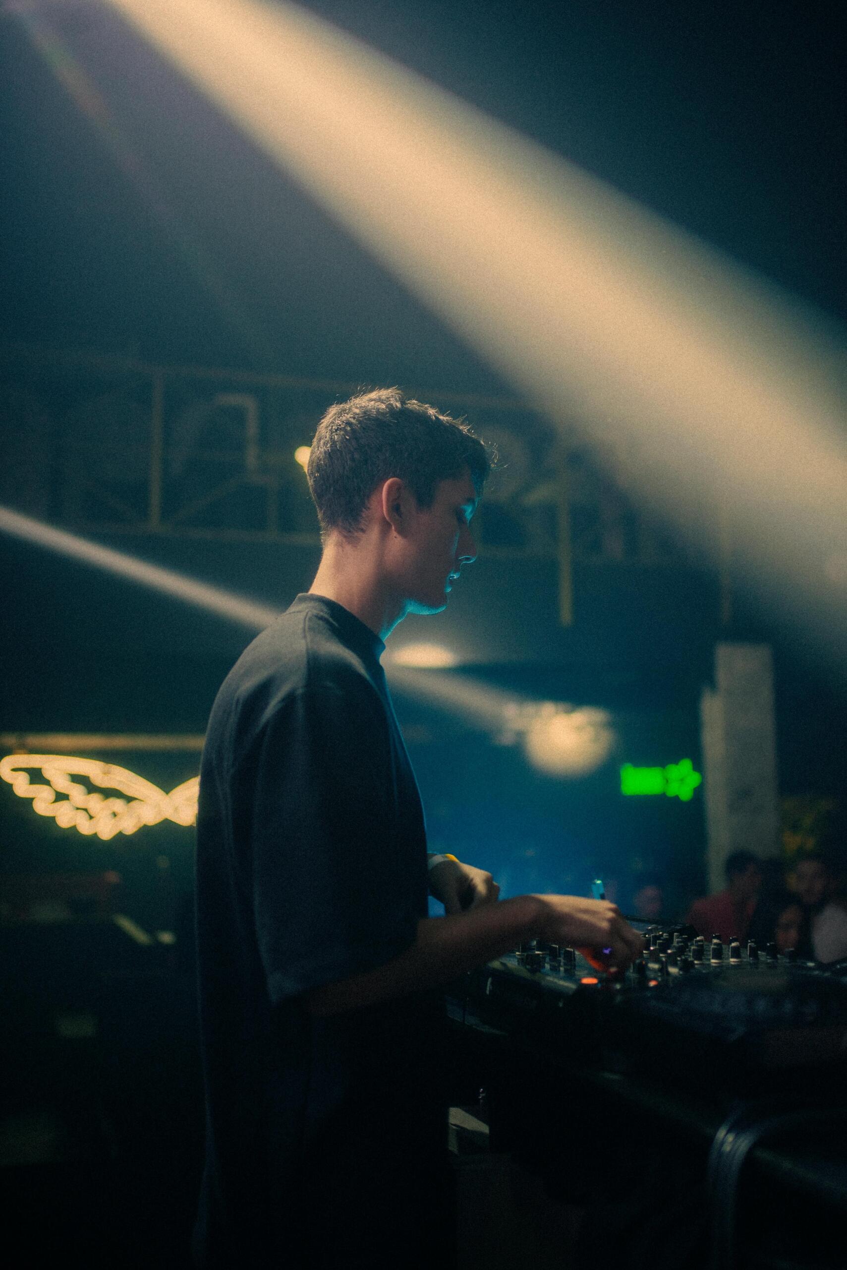 A DJ performing in a club, surrounded by vibrant lights and an energetic crowd.