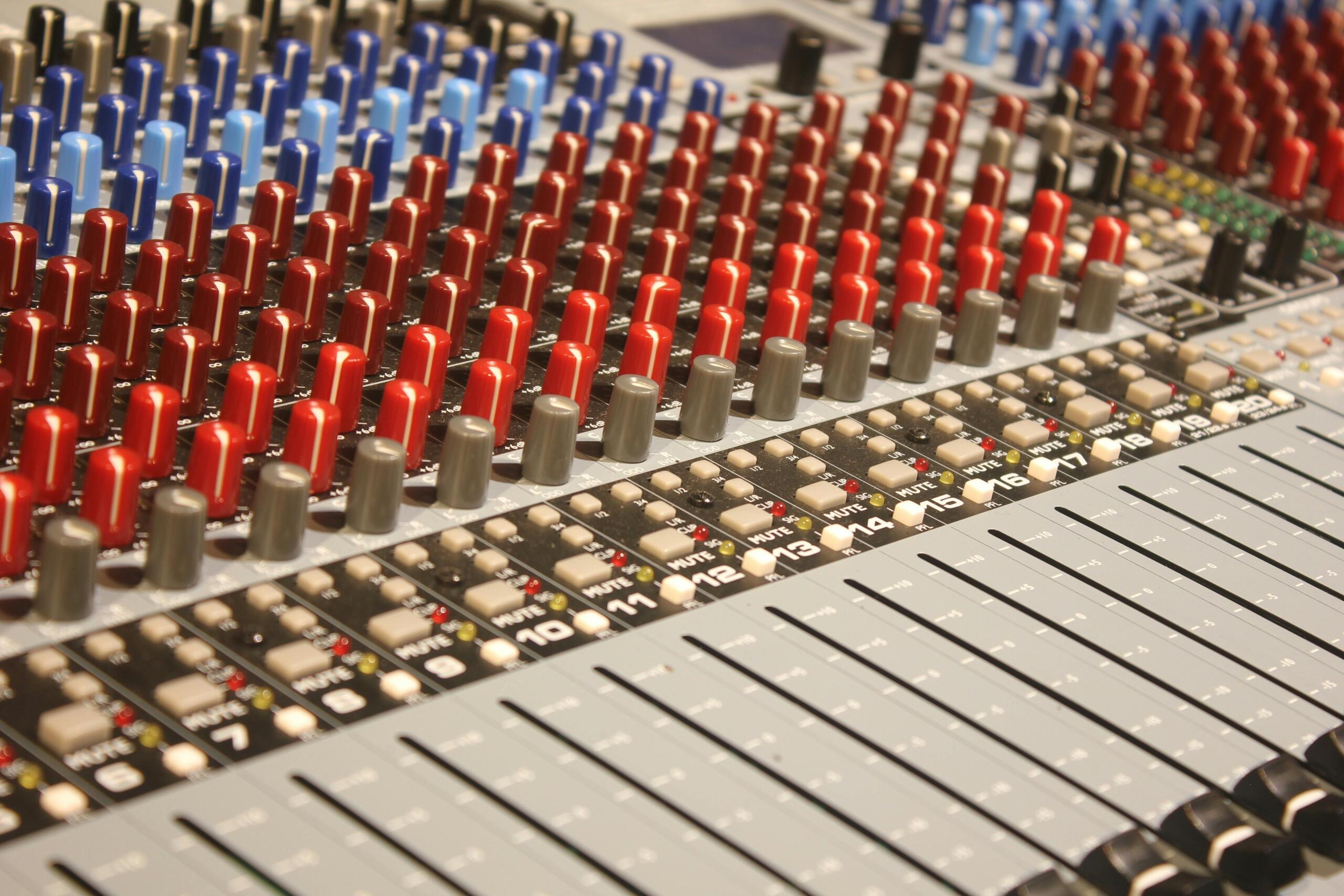 Close-up of an audio mixer with knobs, faders, and LED indicators.