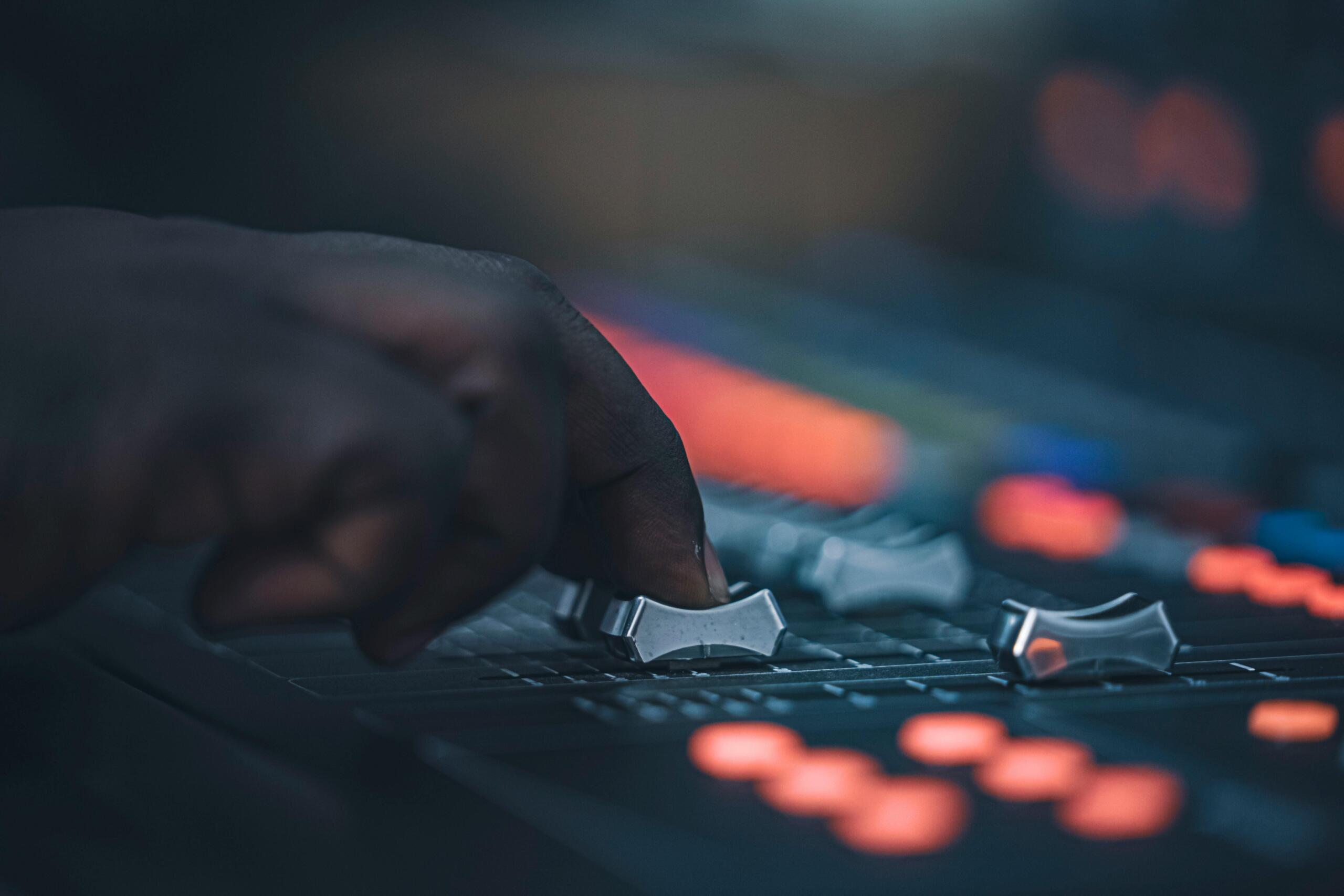Close-up of a hand adjusting knobs and sliders on an audio mixing console.