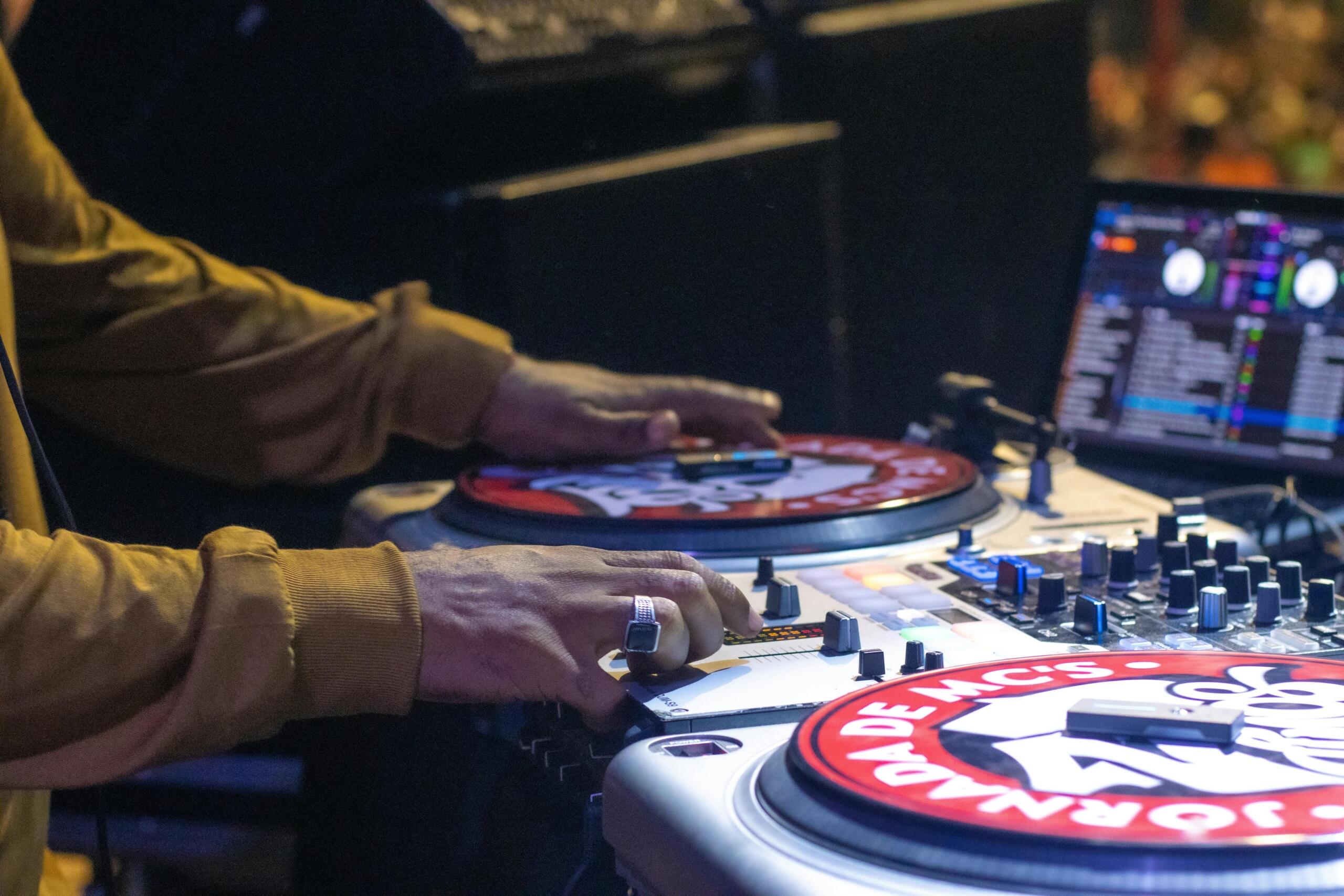 DJ spinning turntables at a live event, with colorful lights illuminating the scene.