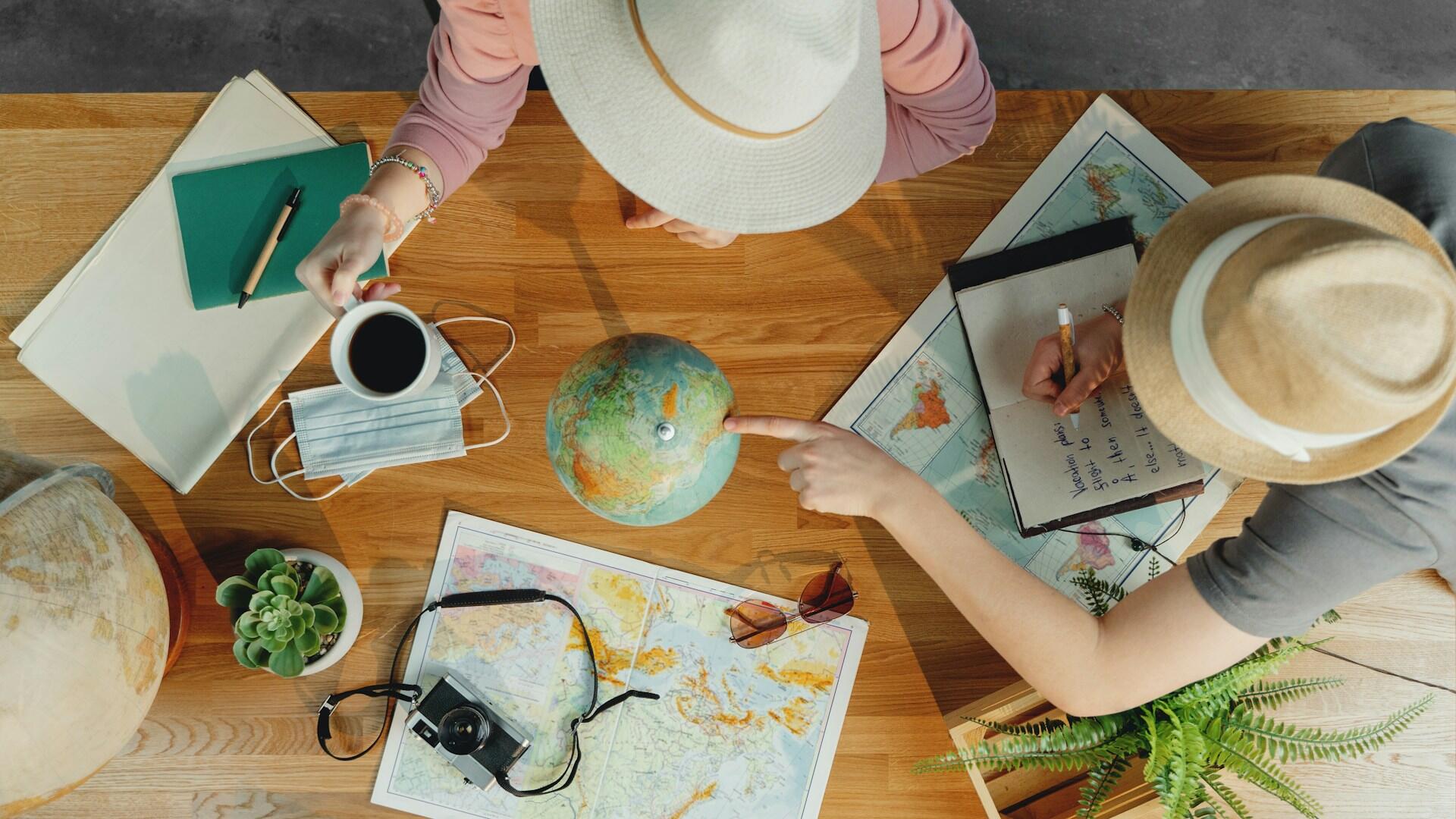 Two geography students at a table, one pointing to a globe and another holding a cup of coffee.