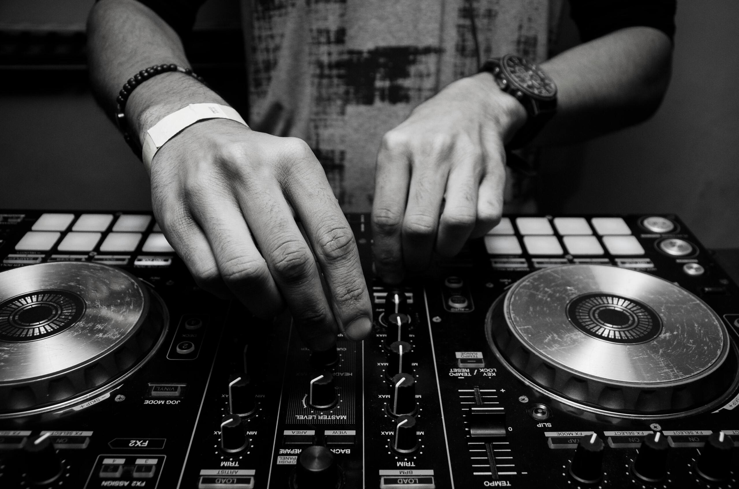 Grayscale photograph of a person operating a DJ controller, adjusting knobs and faders.