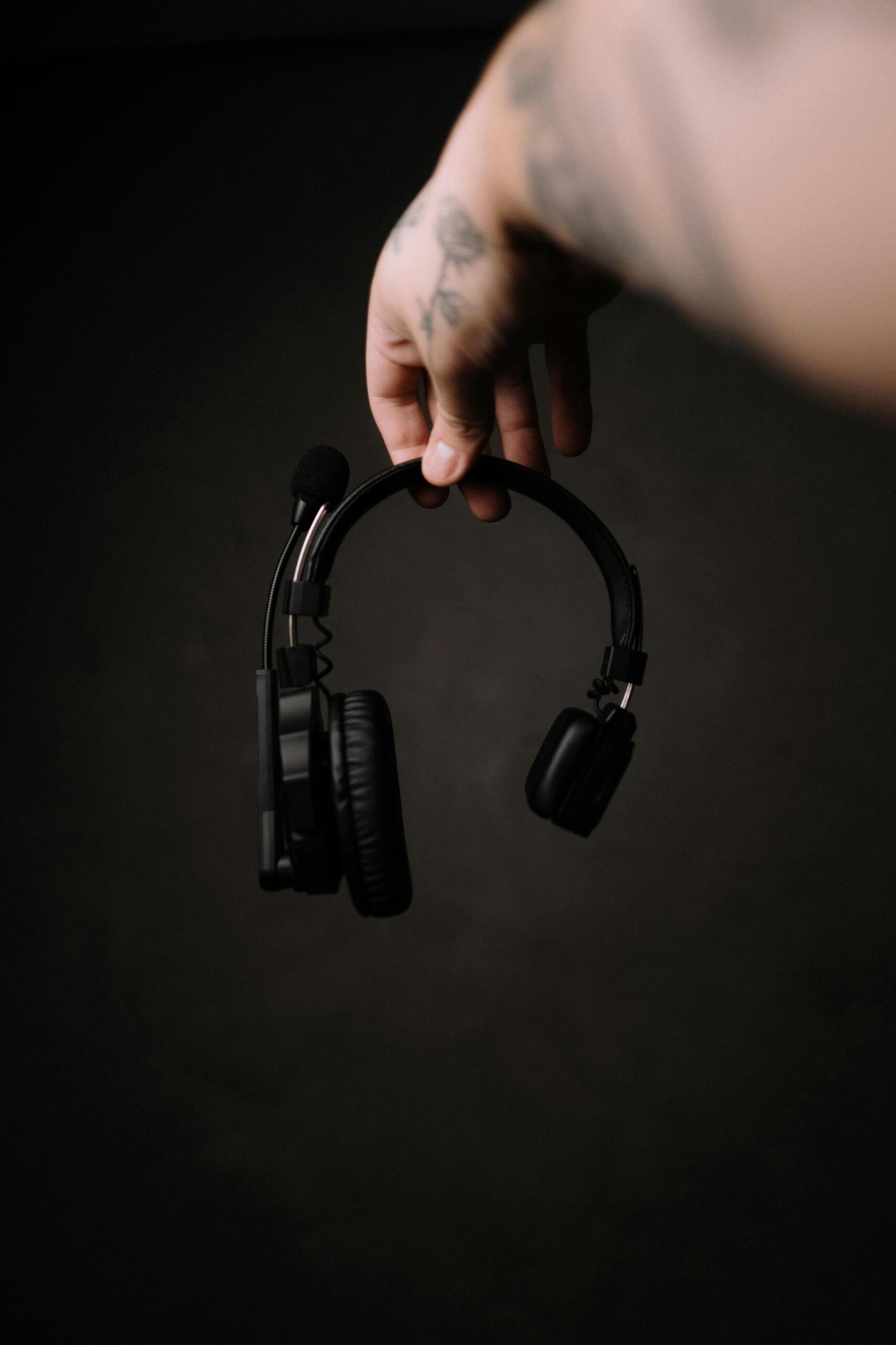A tattooed hand holding black studio headphones in a professional recording environment.