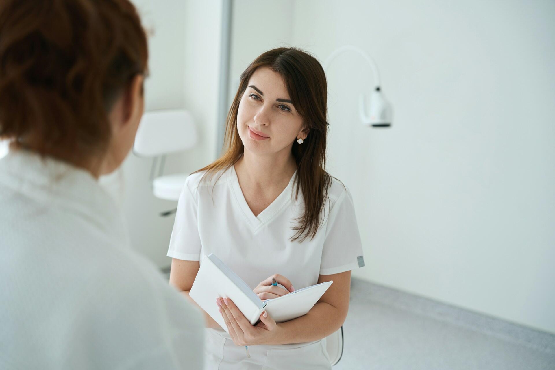 A nurse writing in a notebook, while listening to a collegue.