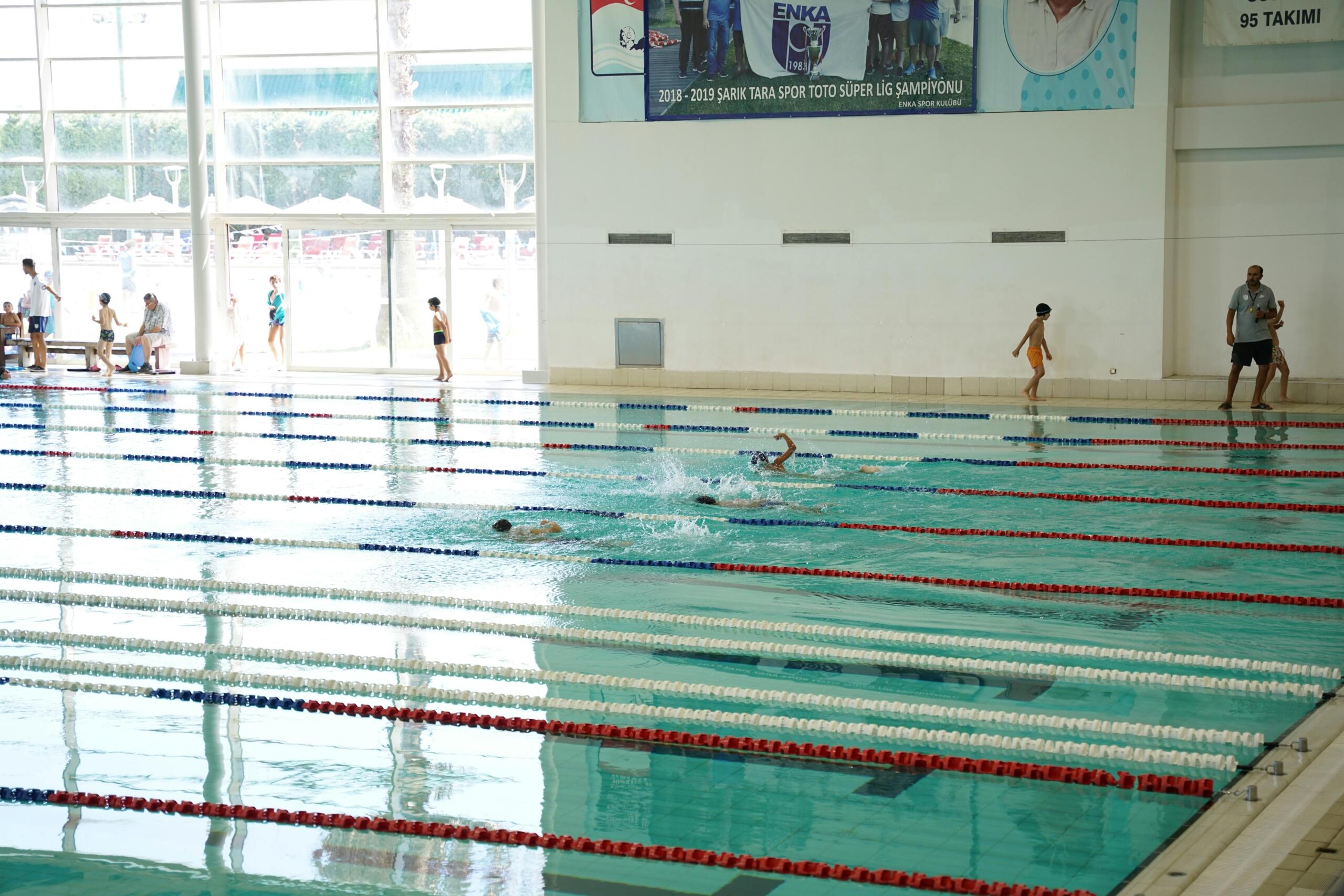 Children practicing swimming techniques in an Olympic-size pool with lane dividers.