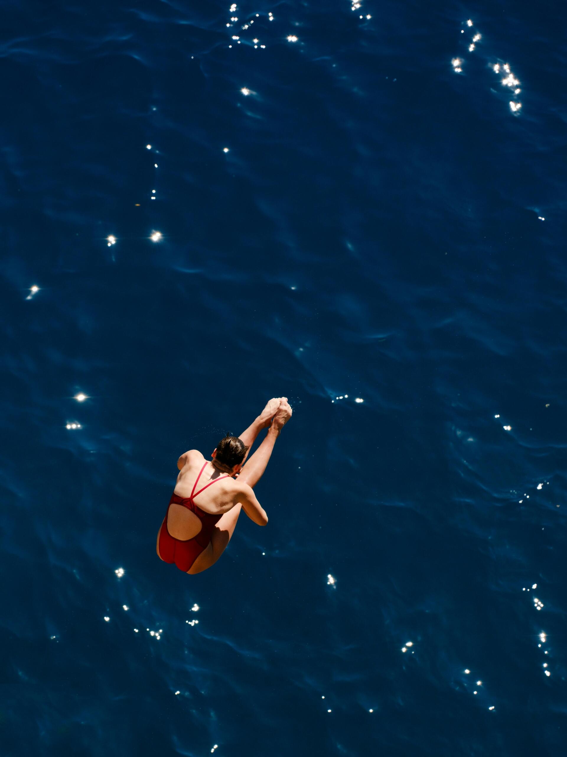 A female diver captured mid-air in a graceful pose above a deep blue sea.