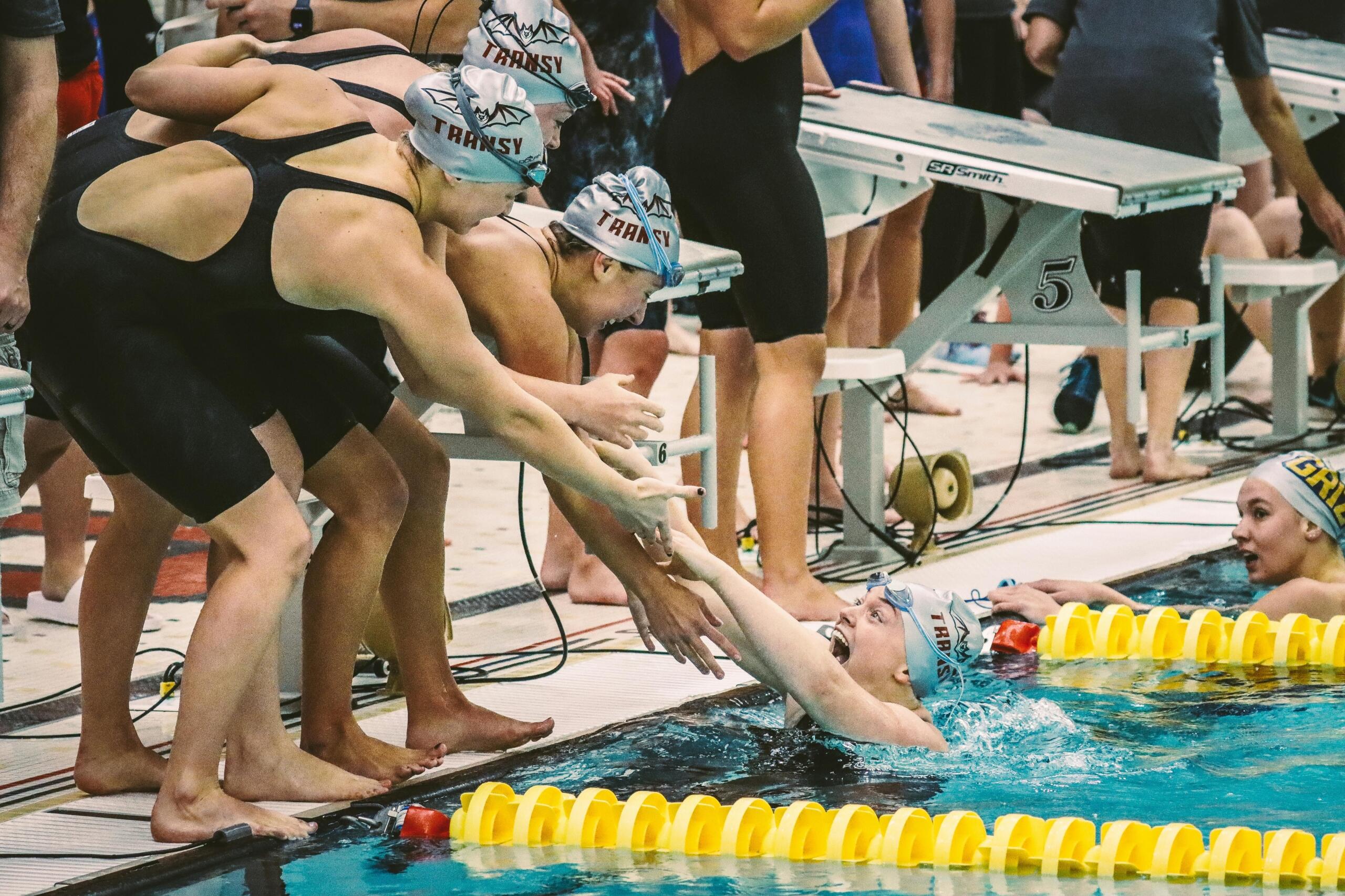 Group of swimmers in swimwear celebrating together by the poolside.