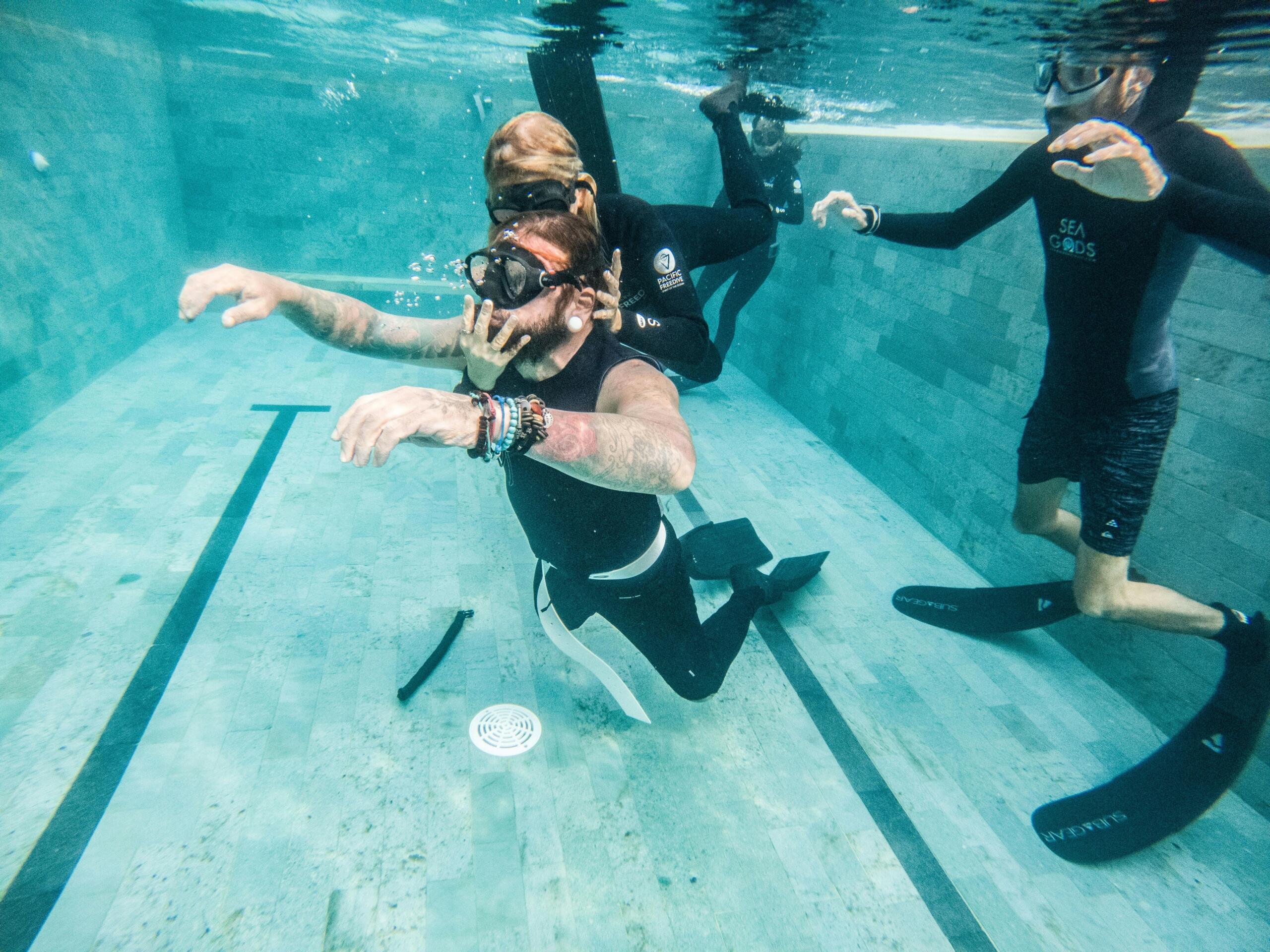 Group of people freediving underwater together in a swimming pool.