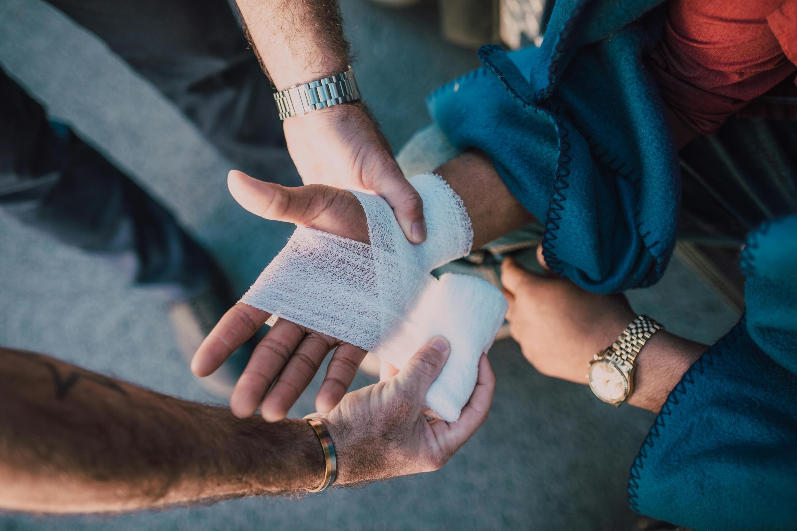 A person applying a bandage to another person's hand beside a swimming pool.