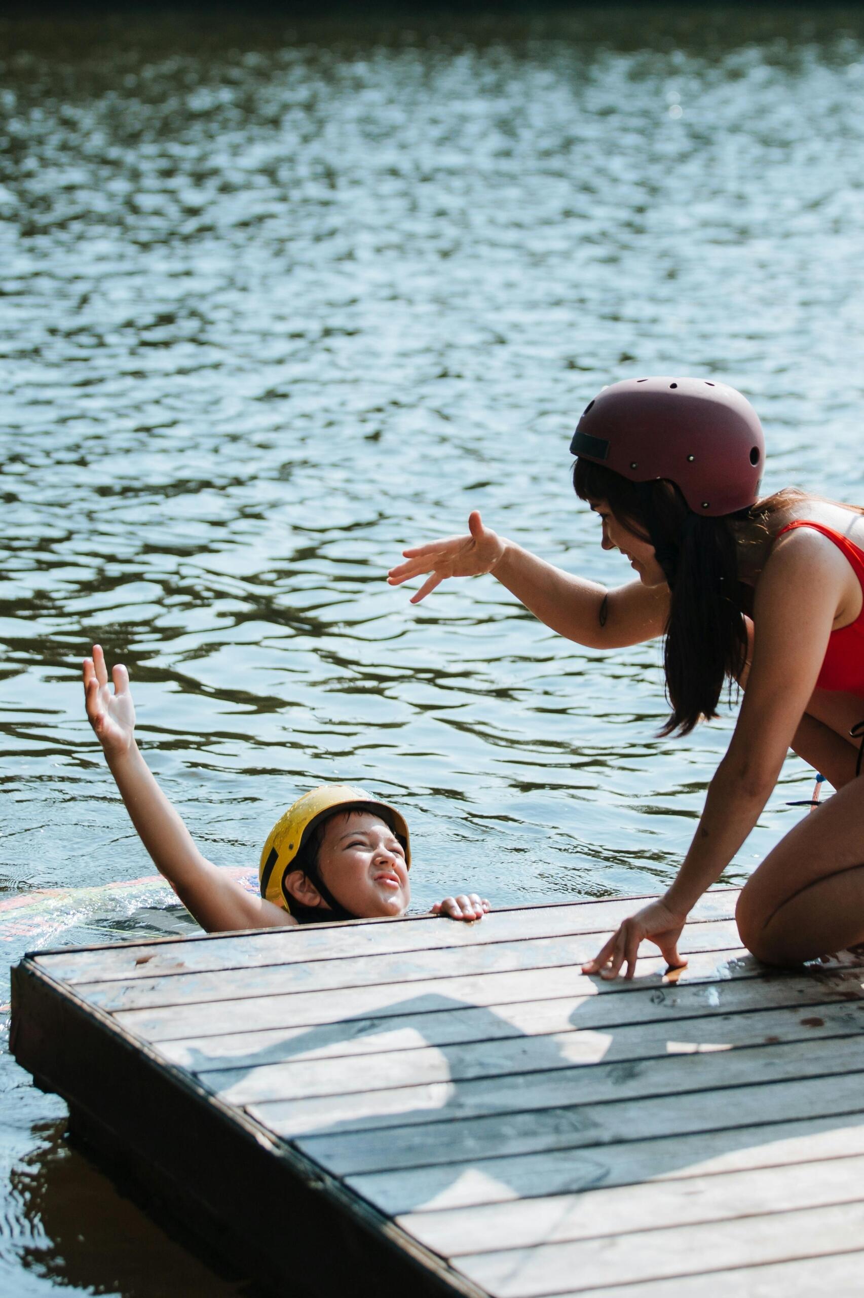 A swimming instructor in the pool high-fiving a young student wearing a helmet in the pool.