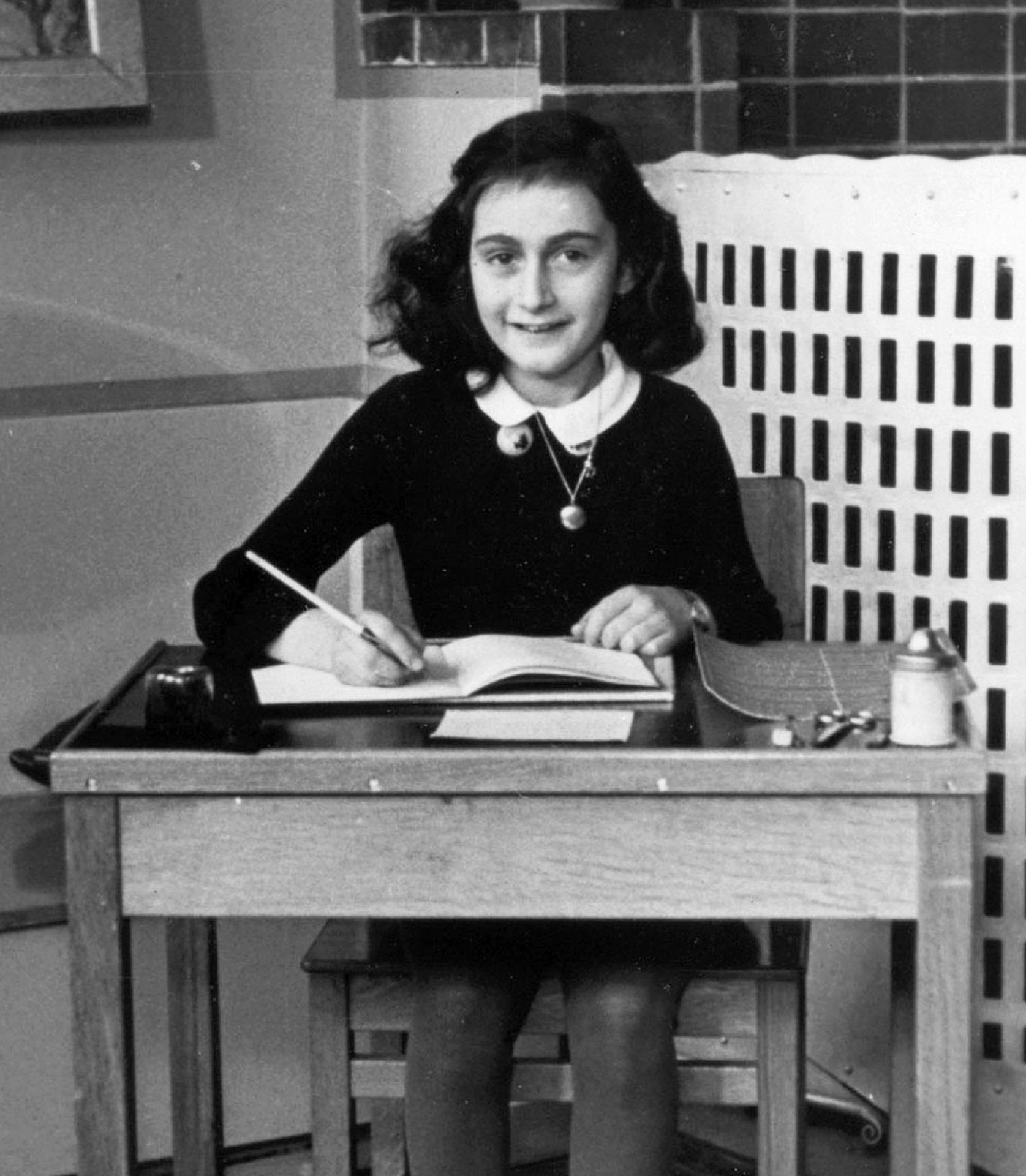 A greyscale image of a girl sitting at a wooden desk with a pencil in-hand. 