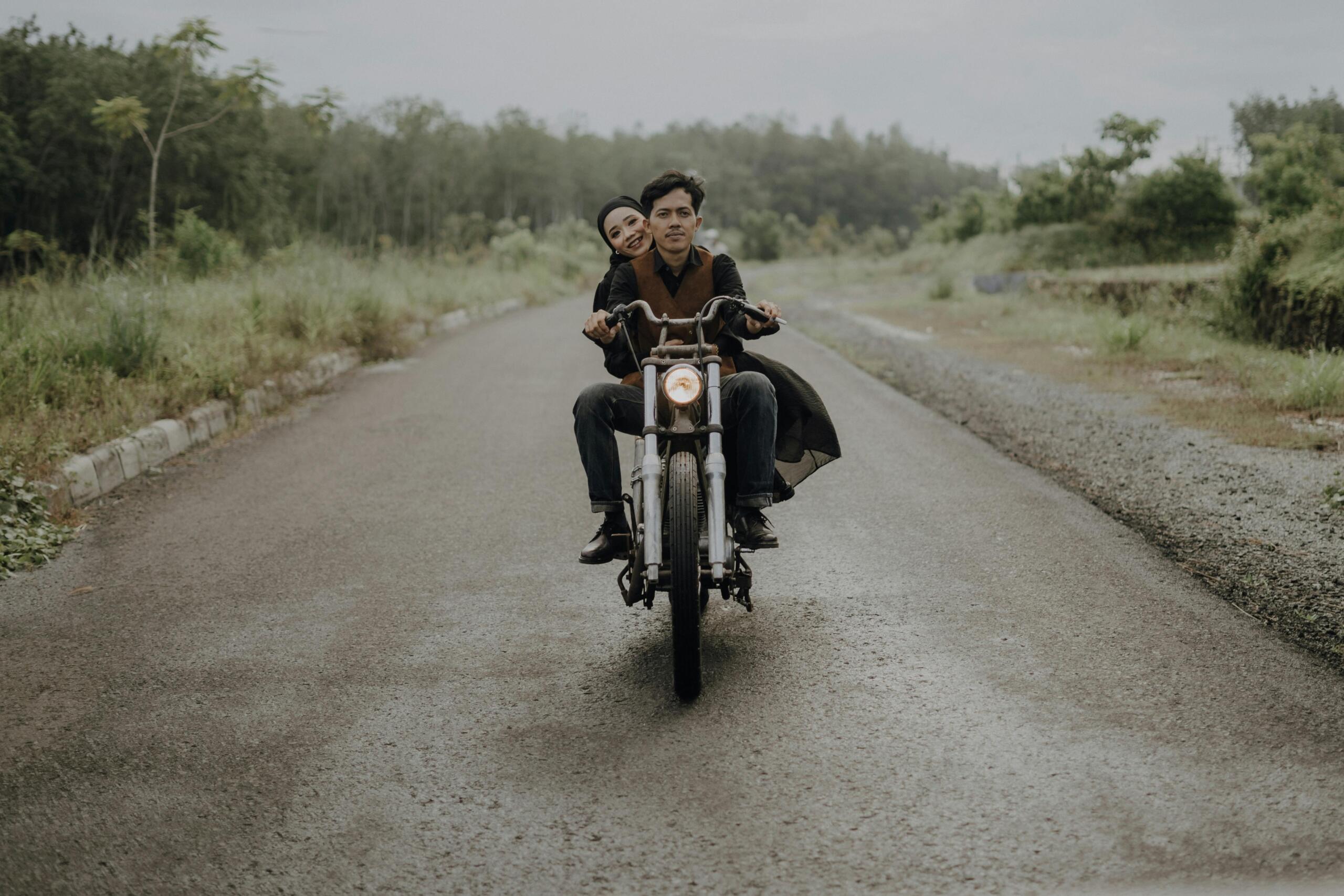 Woman and man riding together on a motorcycle along a road.