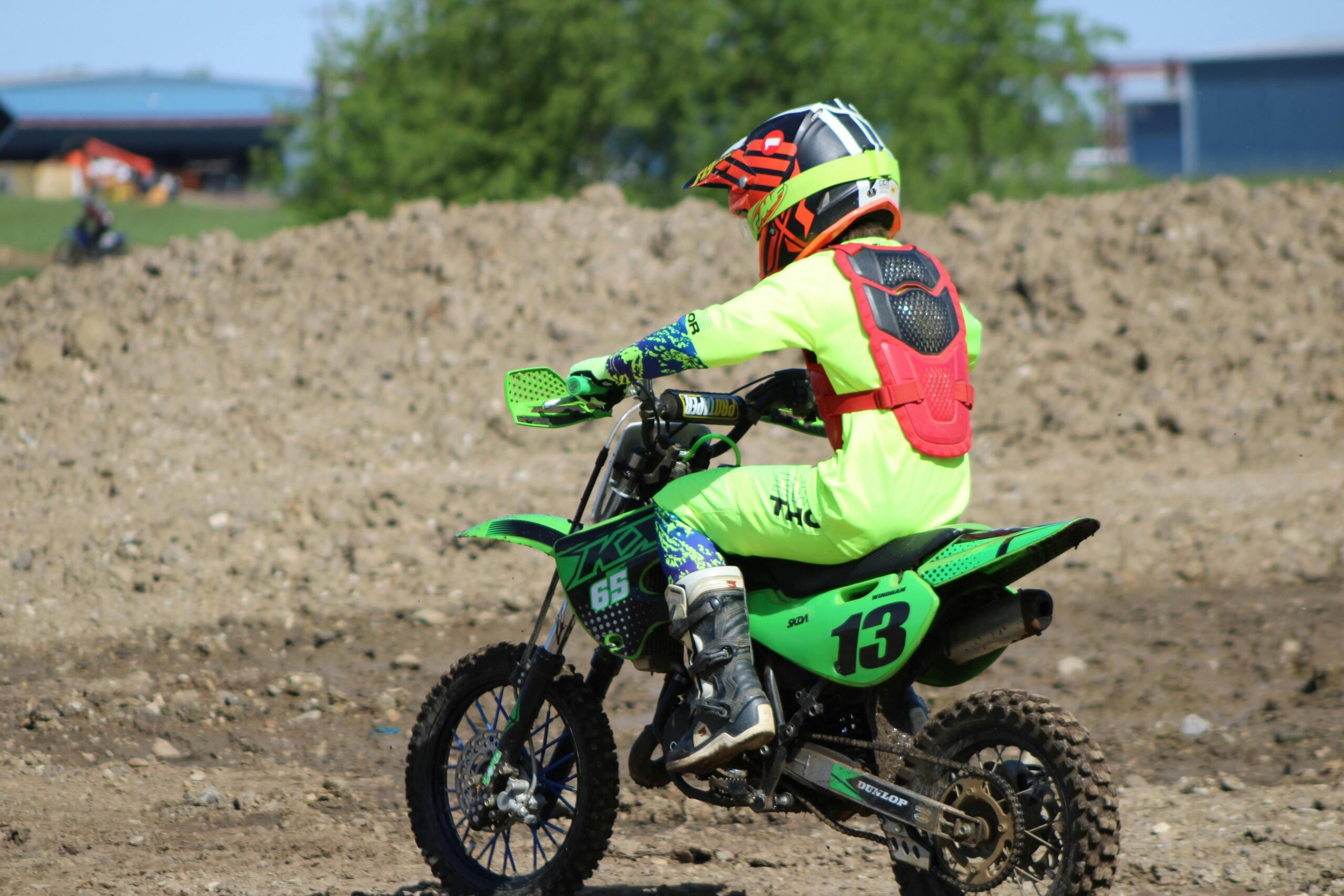 Young rider on a green Kawasaki motocross bike outdoors.