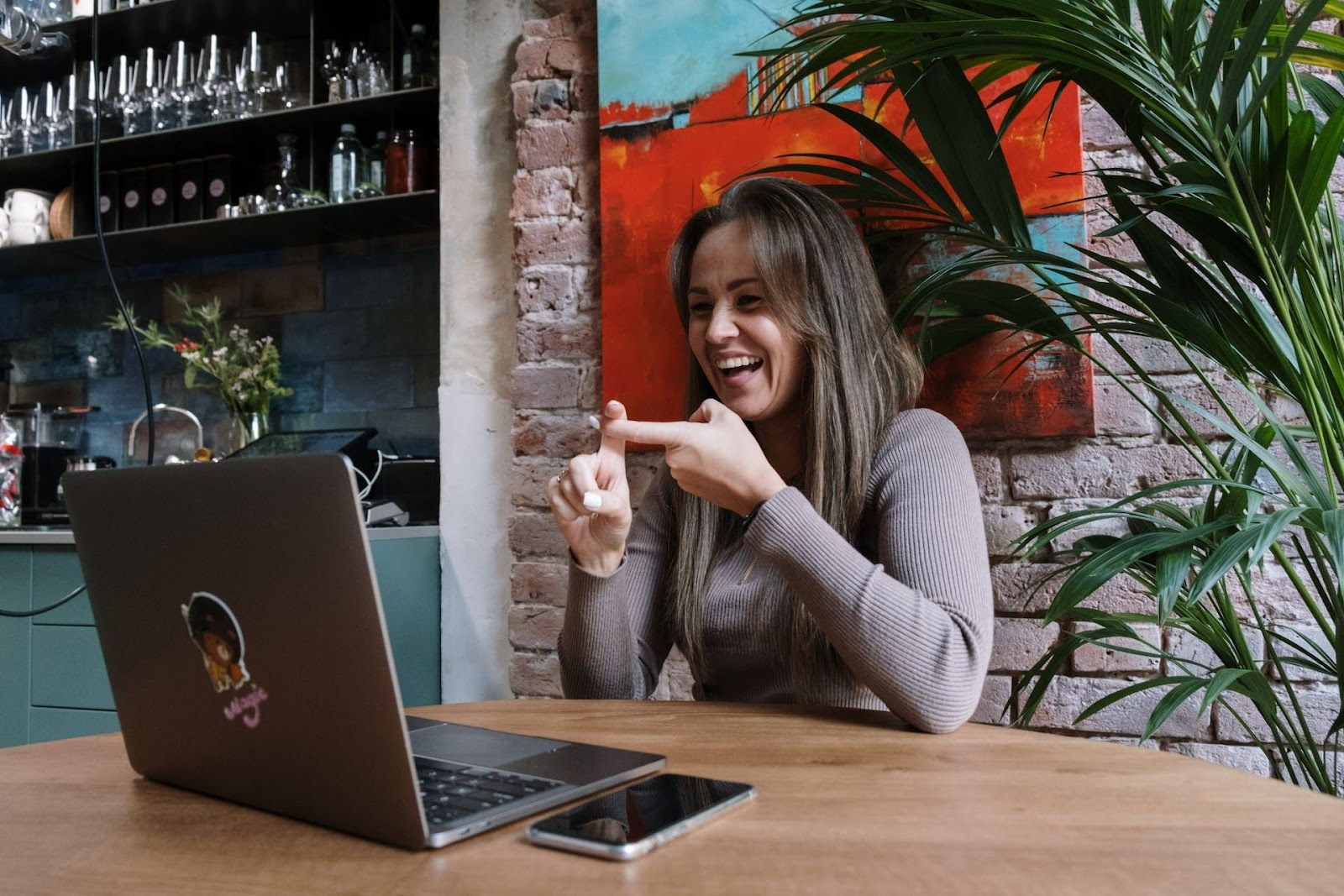 A woman in a grey sweater is communicating to someone by video call in sign language.