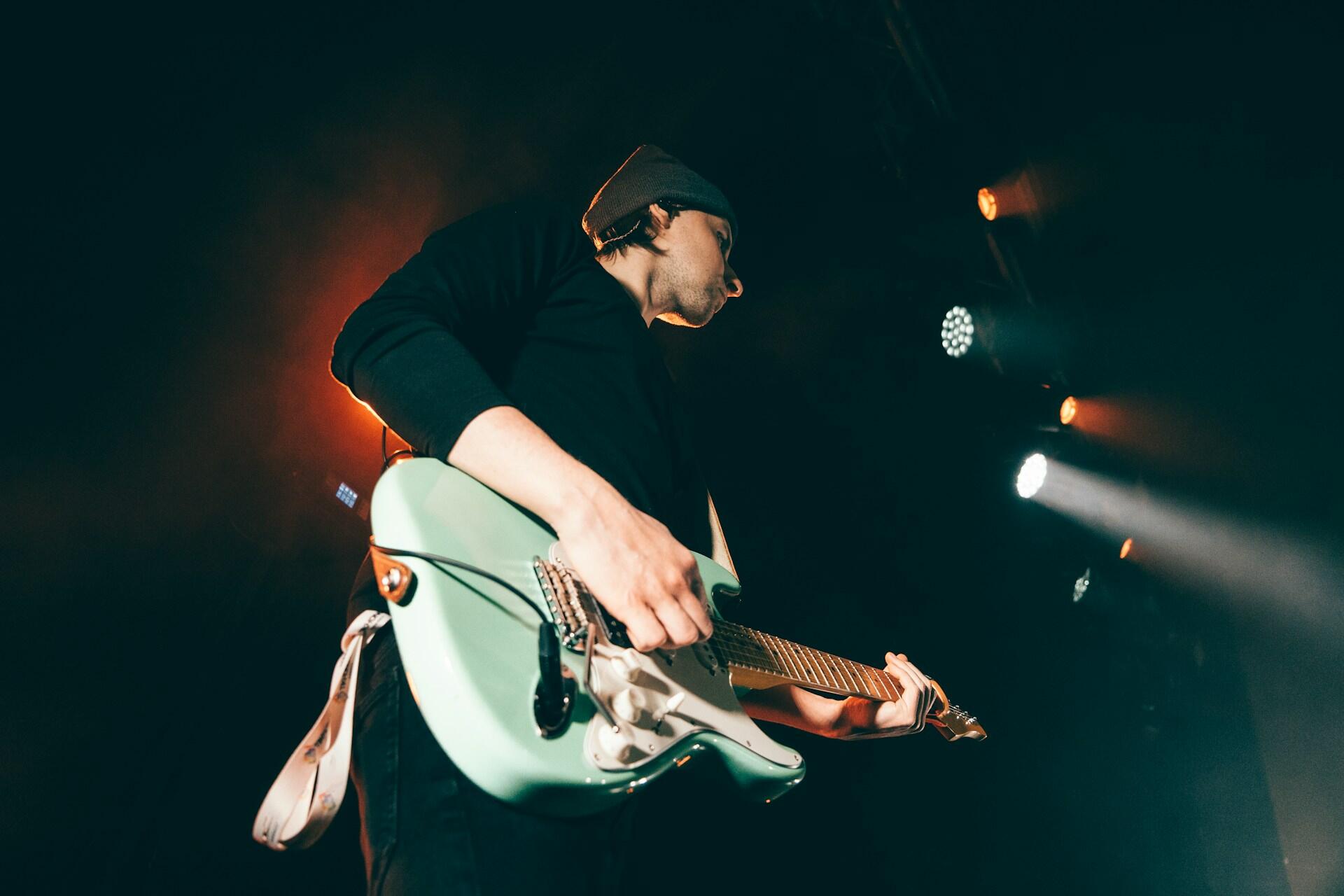A guy on stage playing a blueish green electric guitar.