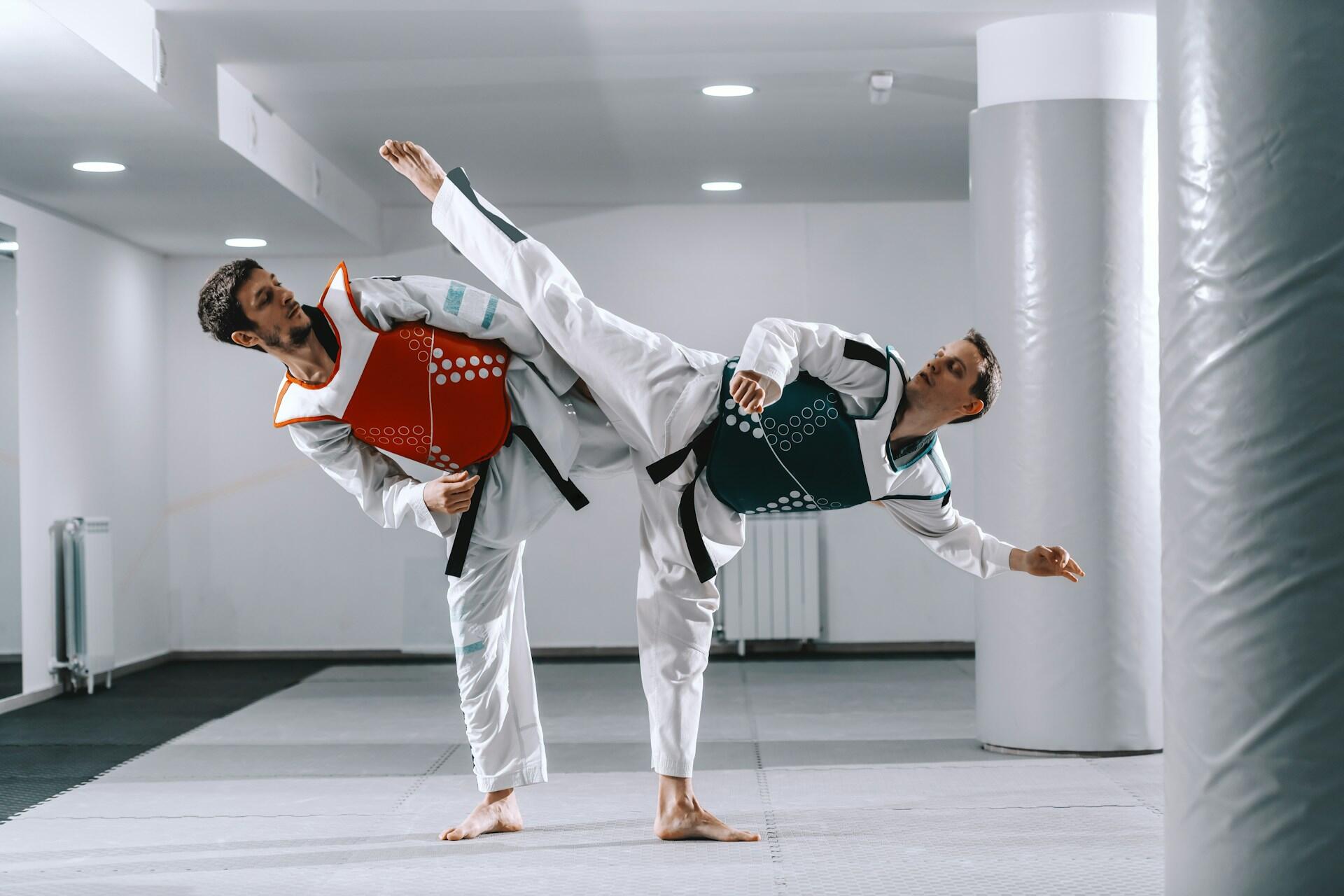 Two men practicing karate moves with one kicking into the air.