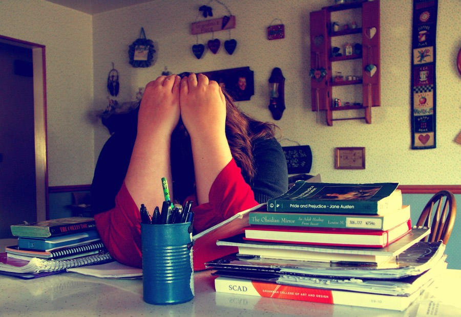 A person in a red and black shirt holding their head in their hands. They’re sitting on a desk with books and a pencil holder in the background. Learning math can be an arduous task for many students if they suffer from math anxiety