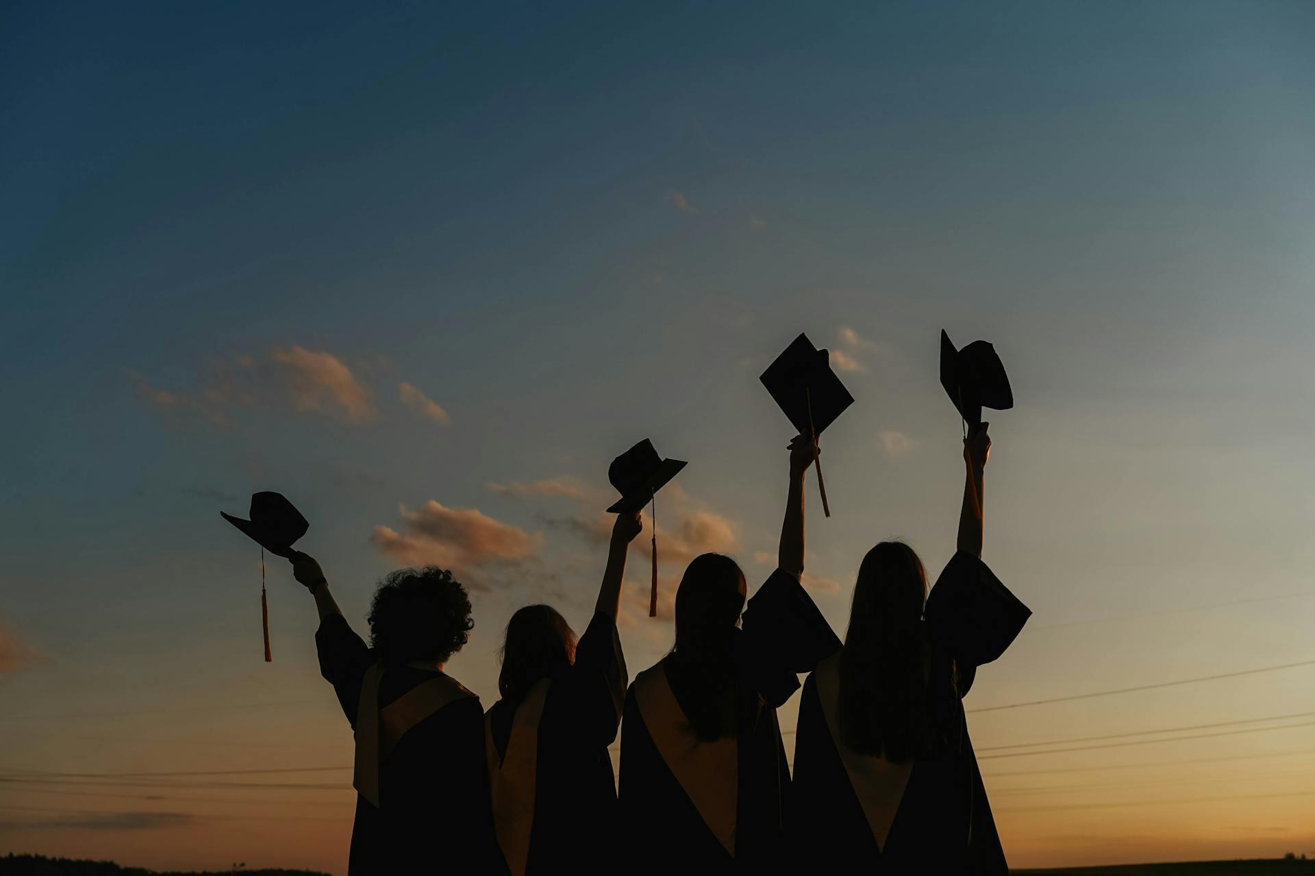 a silhouette of college graduates holding their caps in the air against a sunset sky