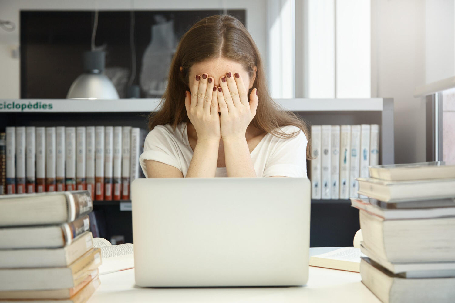 a student sitting at a laptop, covering her eyes in stress