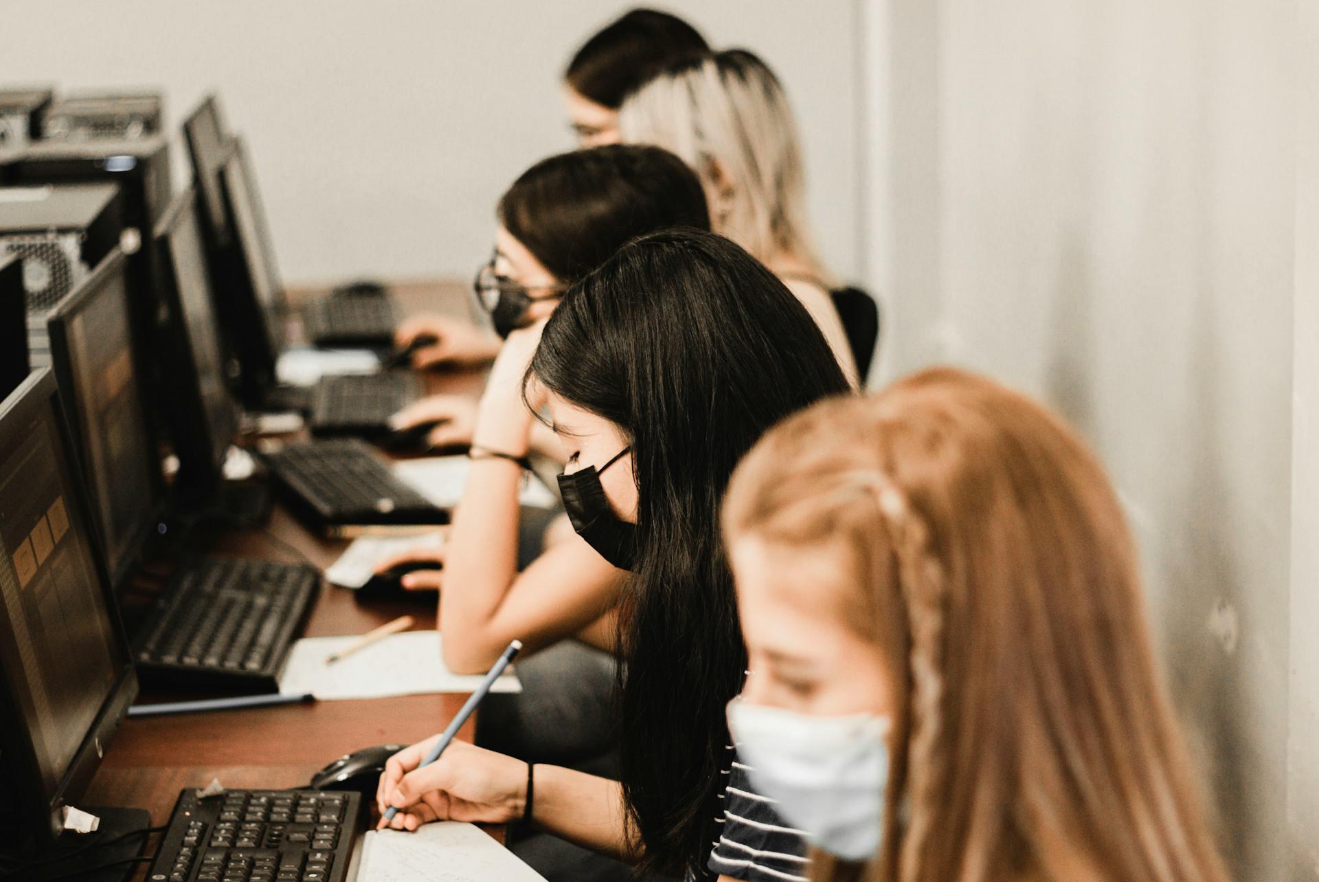 students taking tests at computers with paper nearby for writing notes