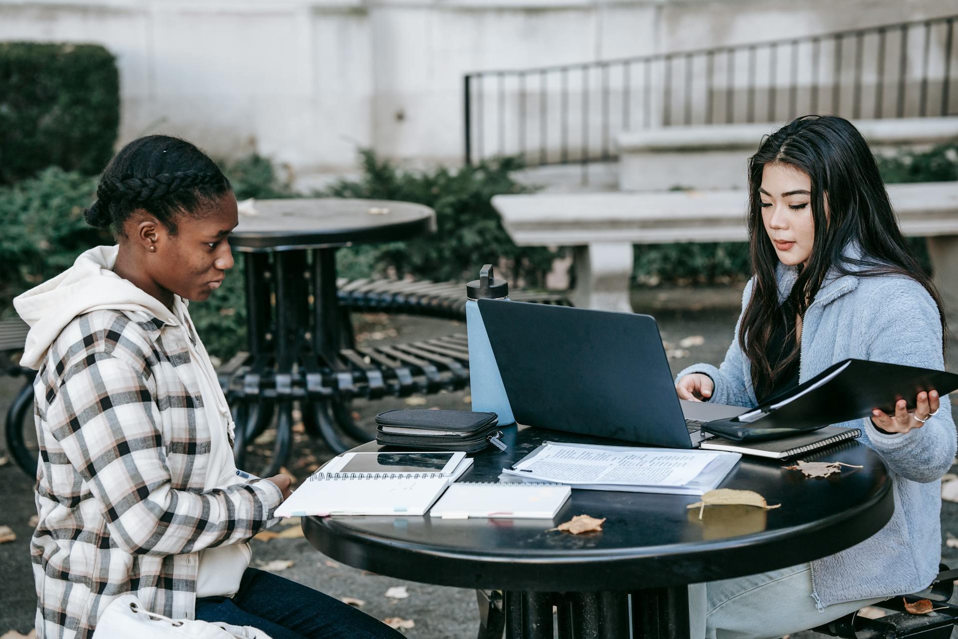two female students studying with notes and a laptop outdoors