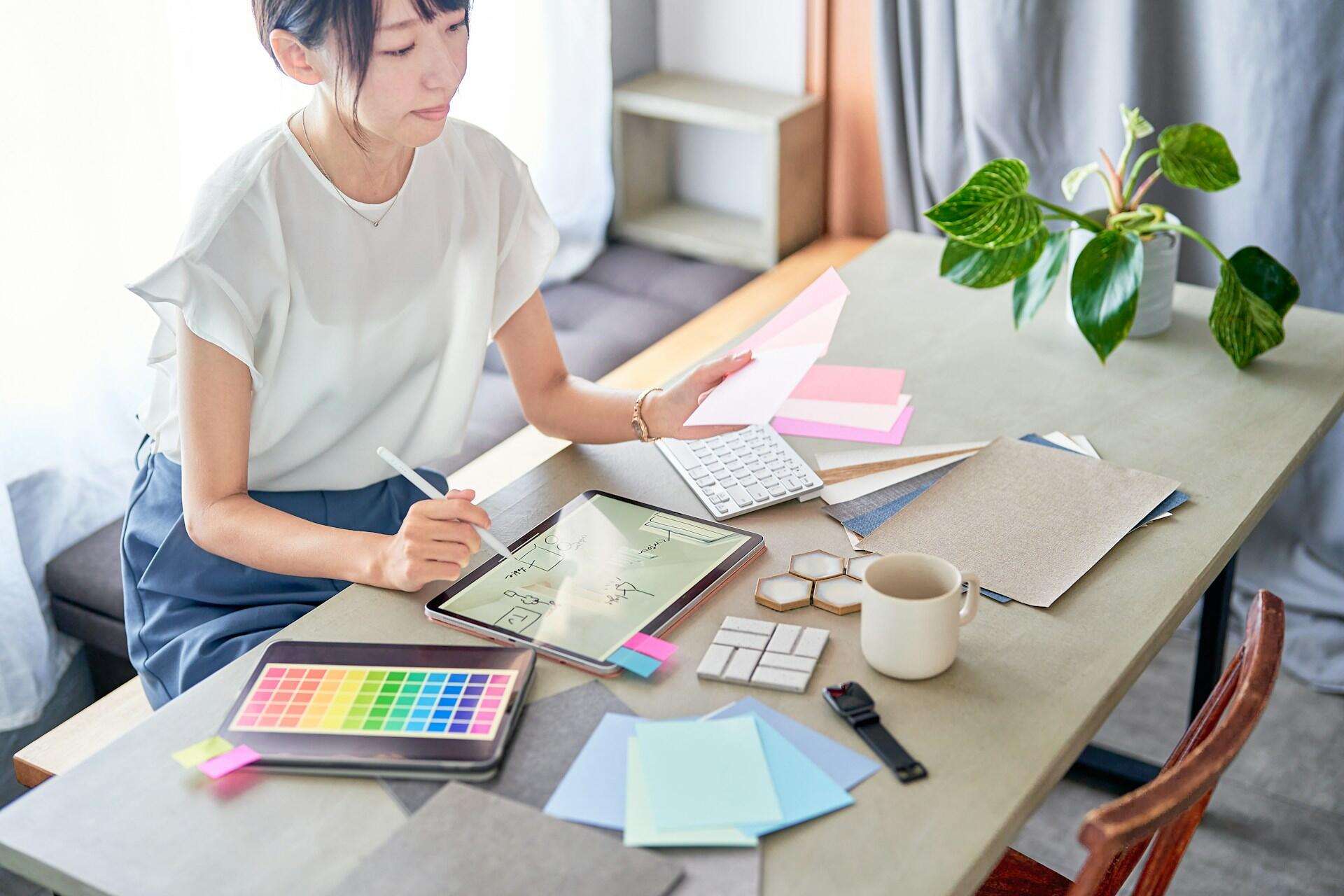 A girl sitting at a desk, reviewing design choices and writing on her iPad.