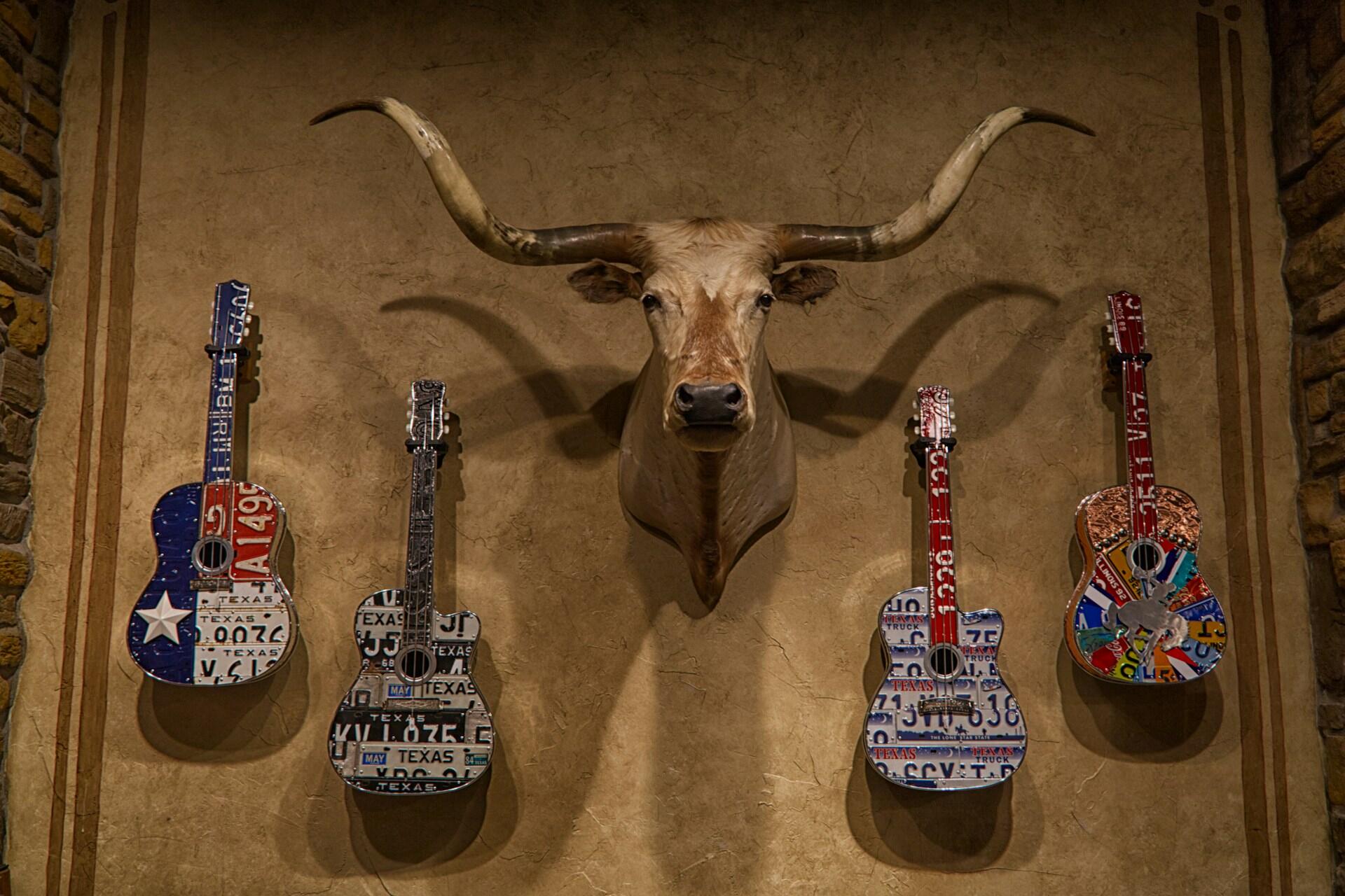 A series of Texas-themed guitars next to a trophy.