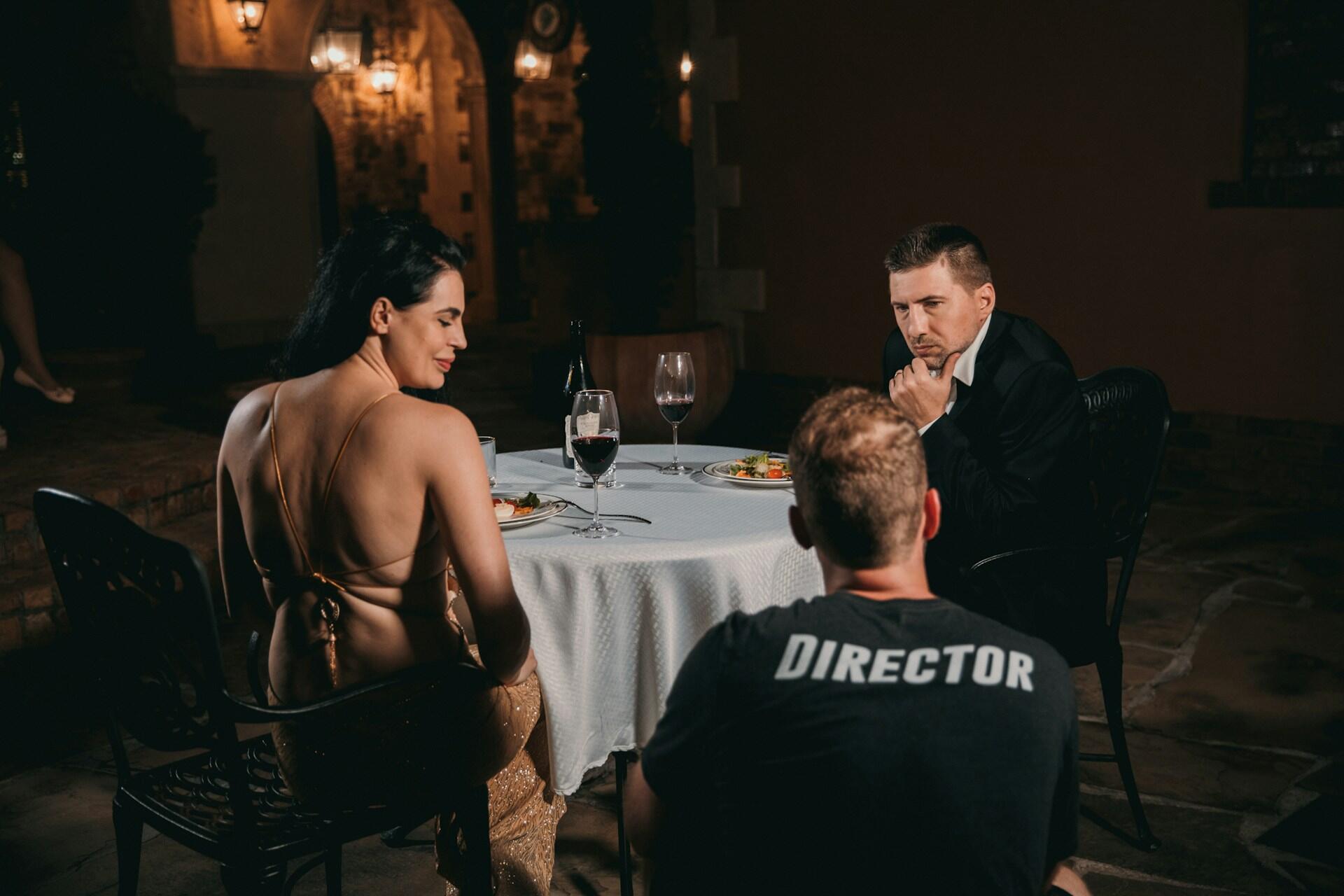 Two actors filming a dinner scene in front of a director.