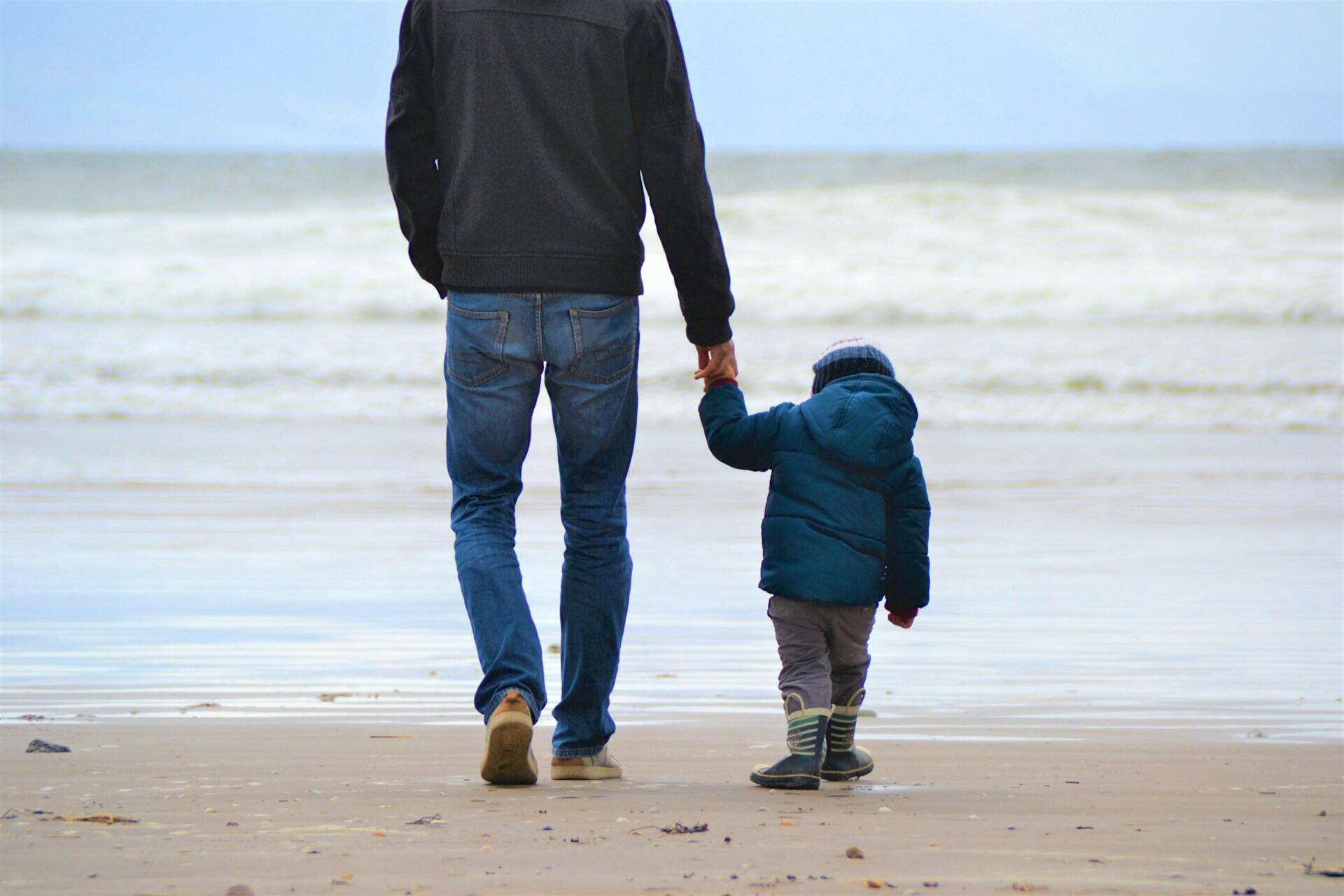 A father holding his son's hand at the beach.