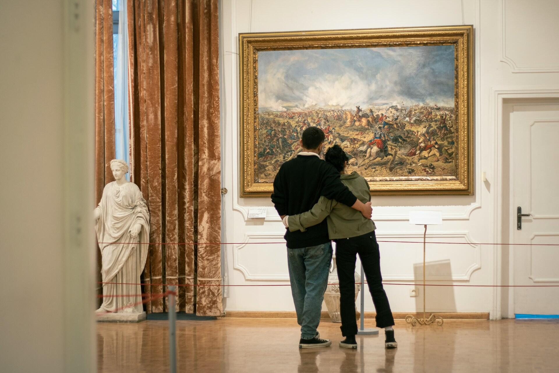 A couple hugging in front of a painting in a museum.