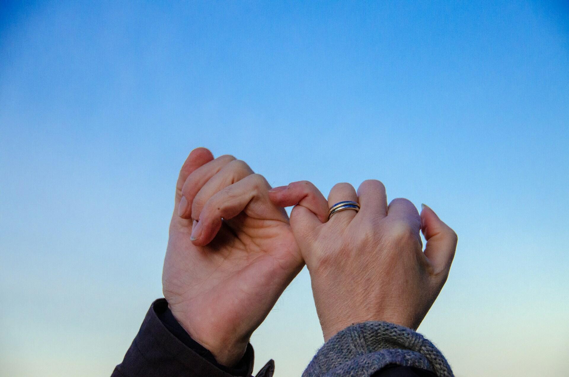 A couple doing a pinky promise in front of a blue sky.