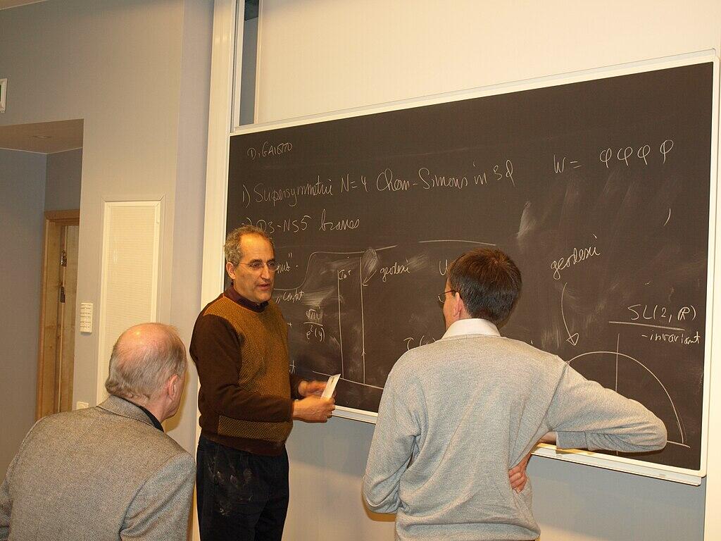 Chalmers speaking with two teachers in front of a chalkboard.