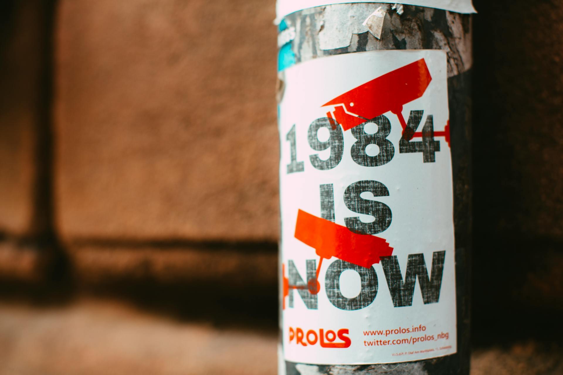 poster on a pole reading "1984 is now" with graphics of surveillance cameras