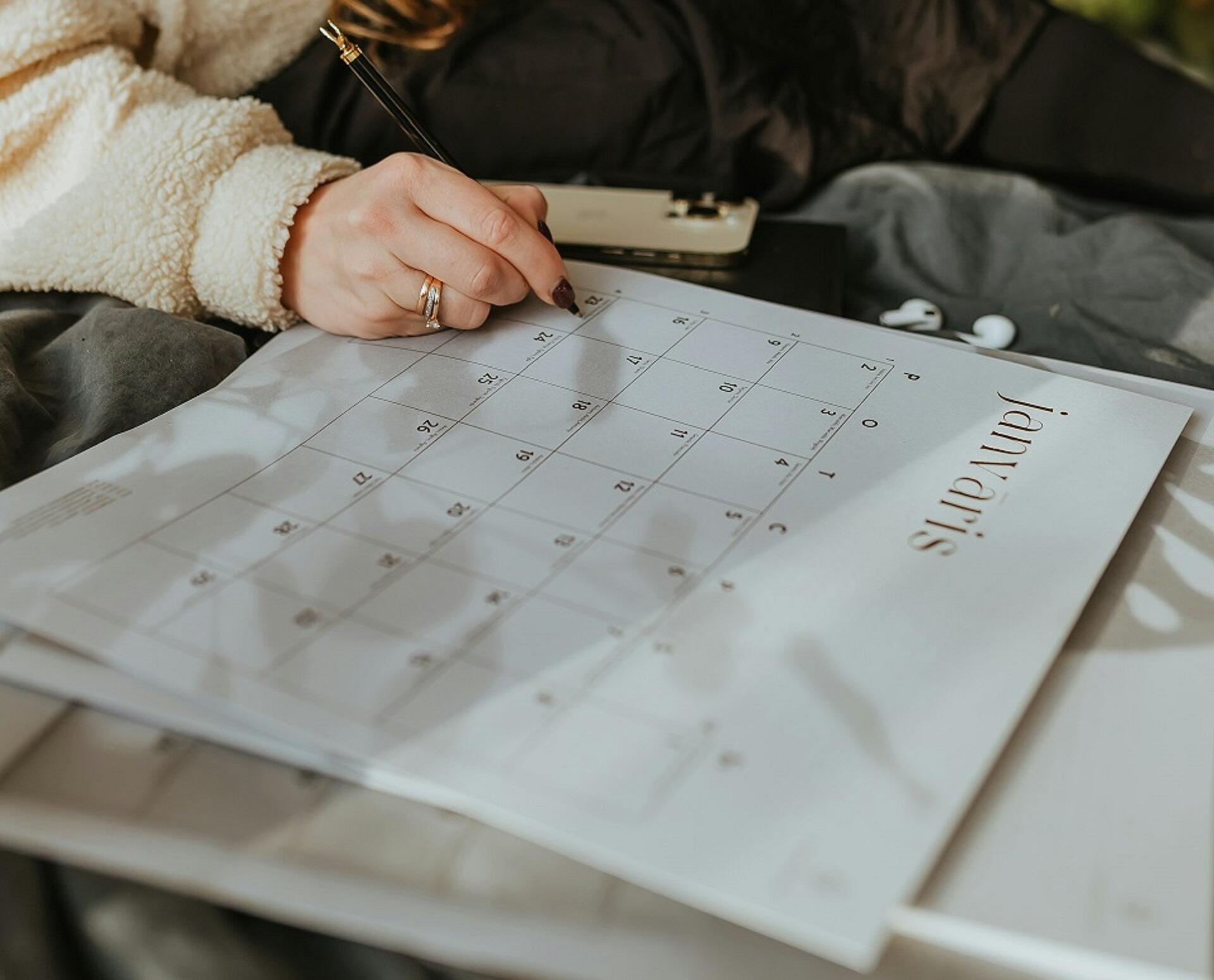 A woman writing on a large calendar. 