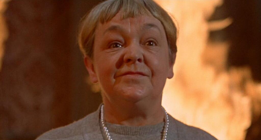 film still of older woman with flames in the background