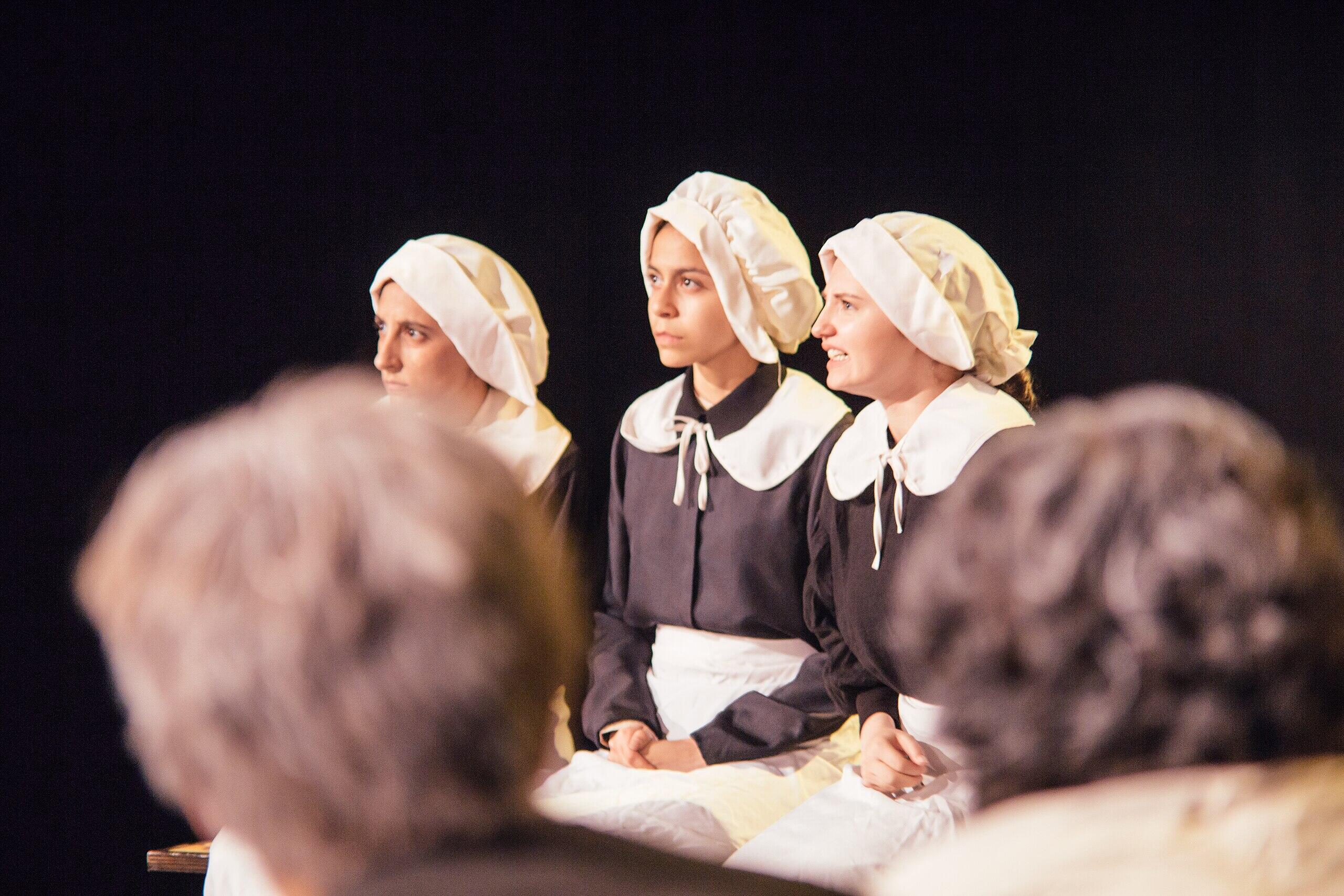 a photo of three girls dressed in Pilgrim costumes as part of The Crucible stage production