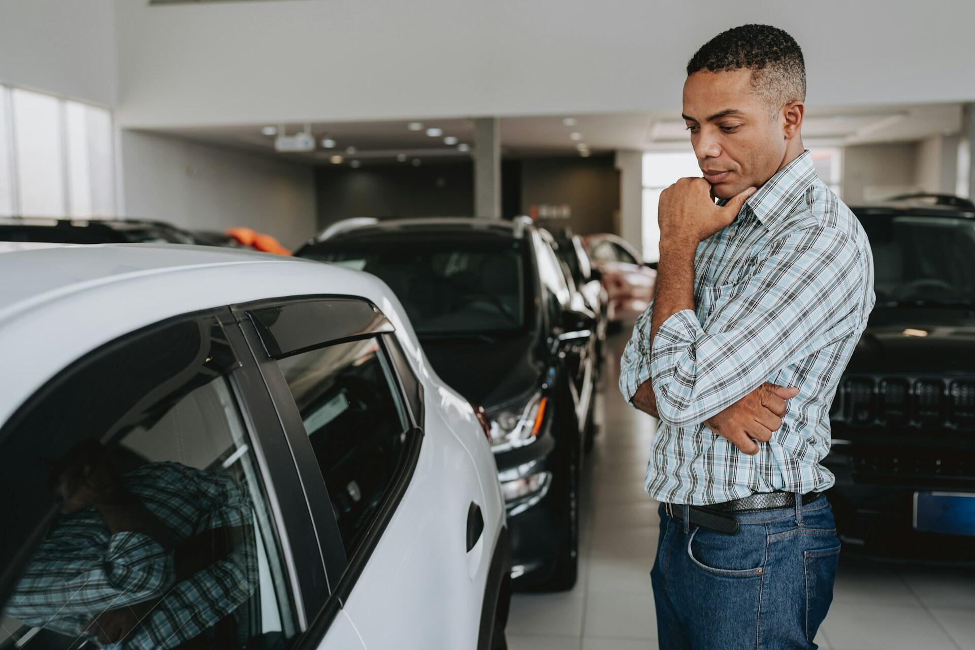 man contemplating a new car in a dealership showroom