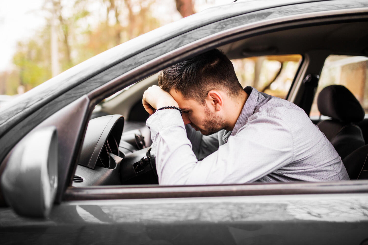 man in car looking frustrated resting head on steering wheel