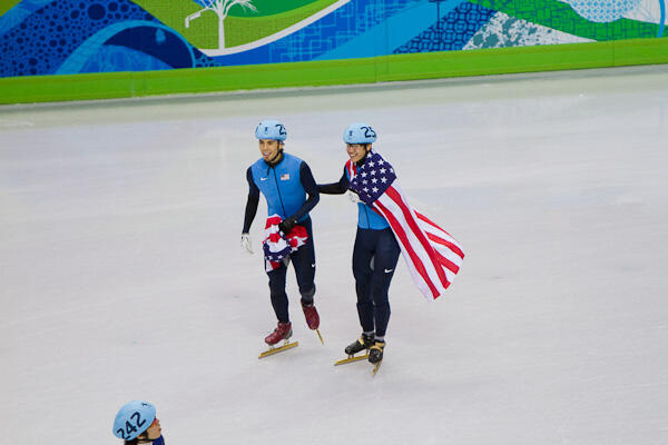 Apolo Ohno and a teammate on the ice holding the American flag.