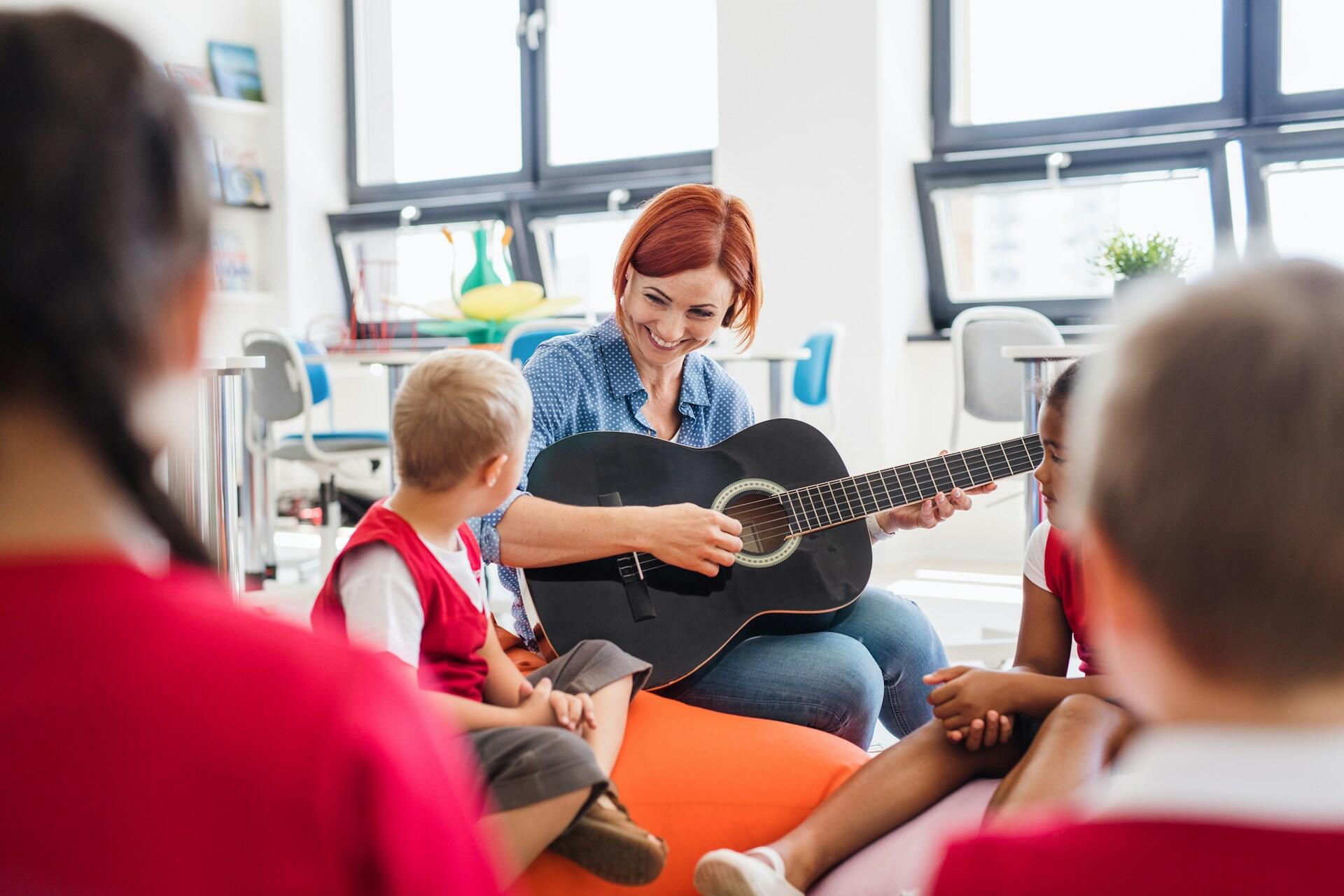teacher playing guitar for class of young students